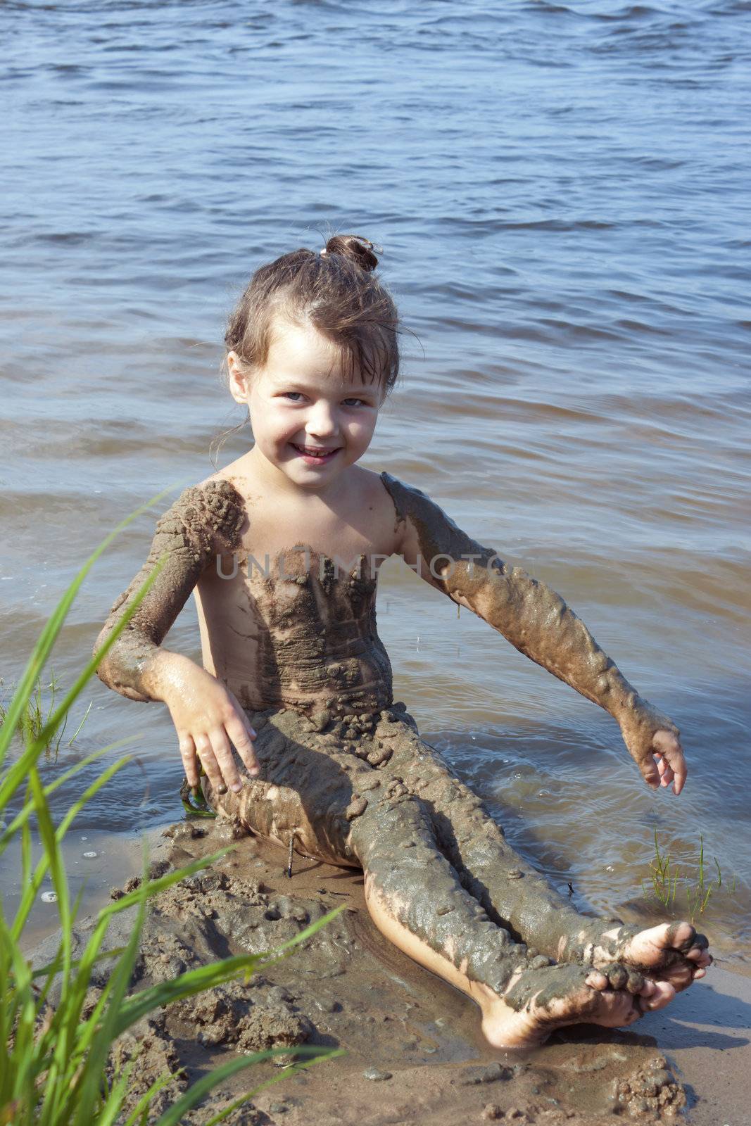 Naughty baby girl in the mud on the river