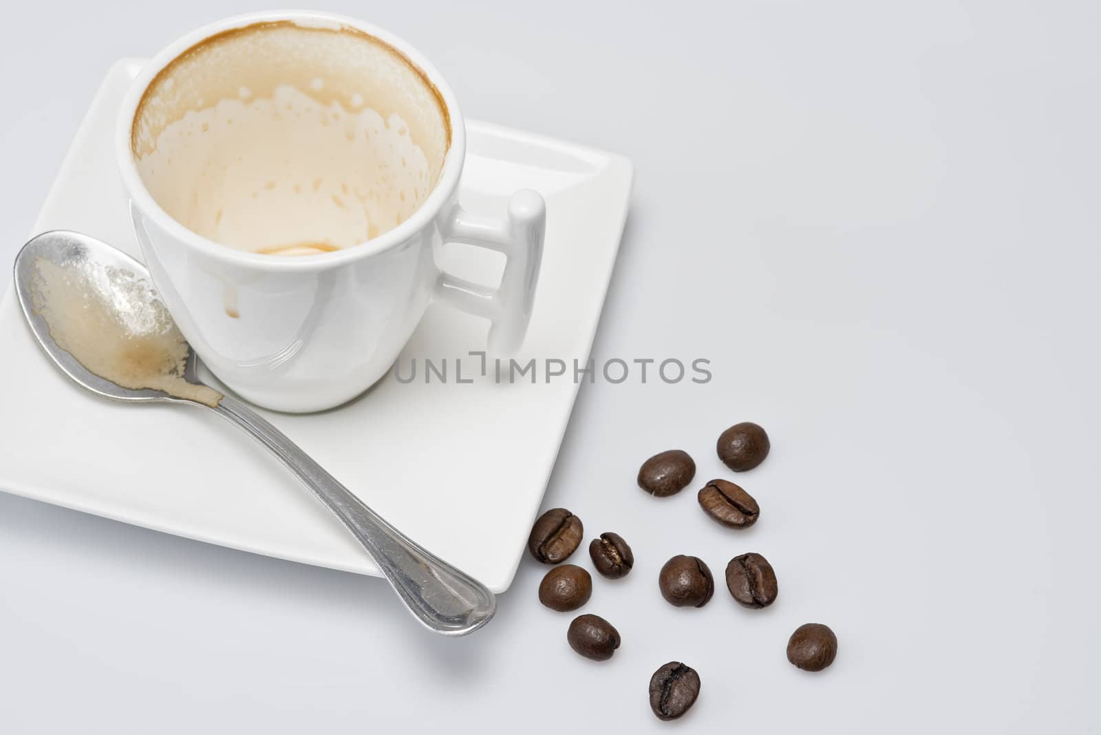 An empty cup of coffee and some coffee beans.