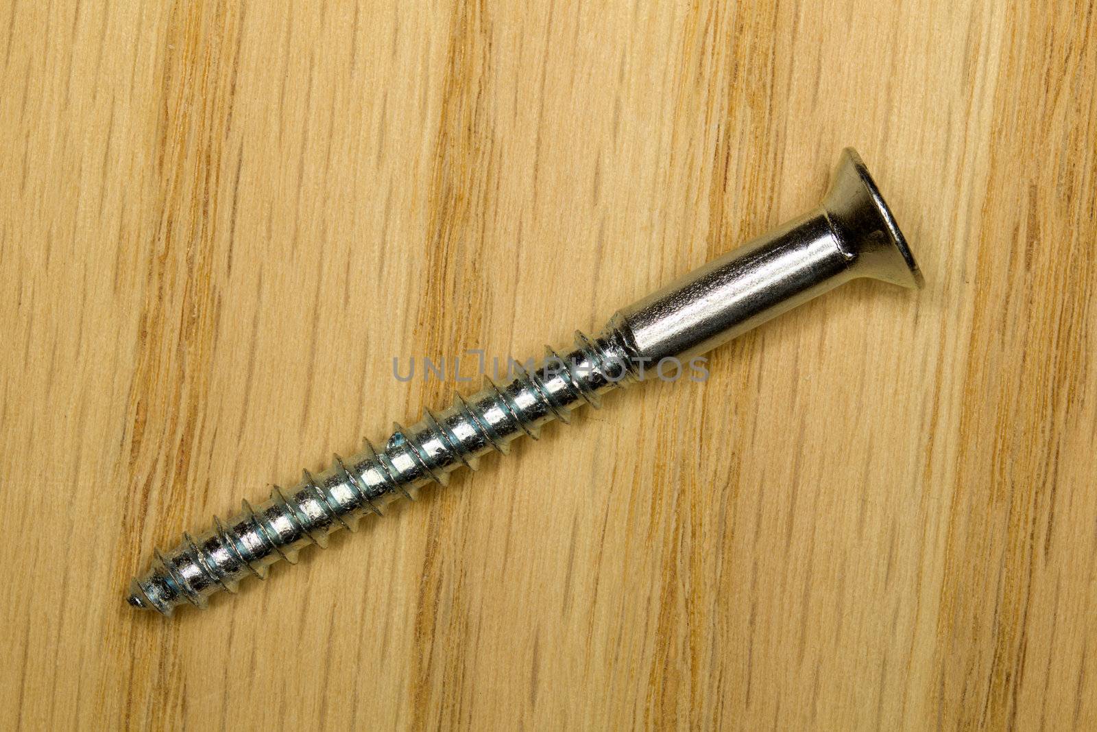 Side view of a silver steel screw laying on a piece of timber in macro