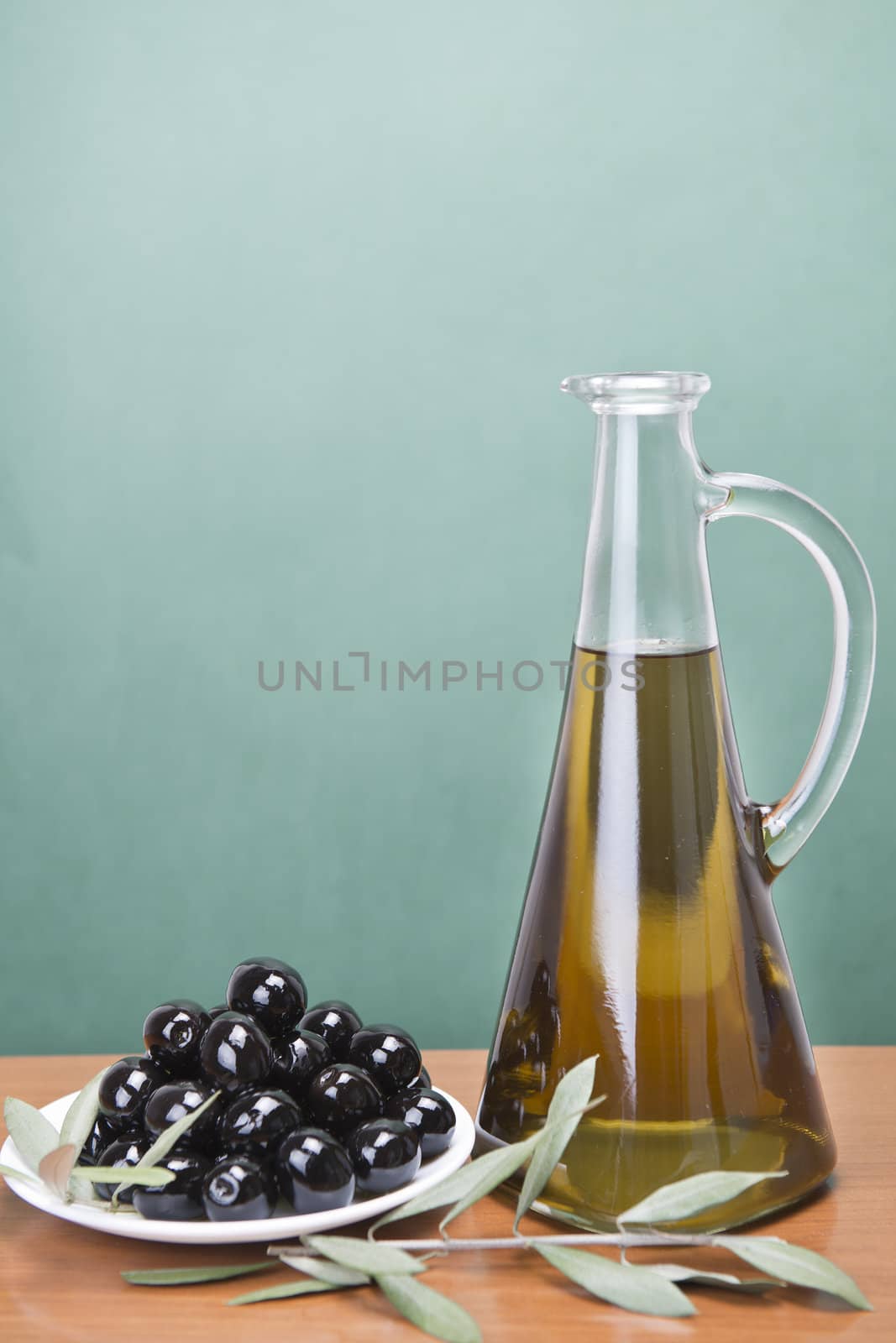 A jar with olive oil ans a plate with black olives on a wooden surface.