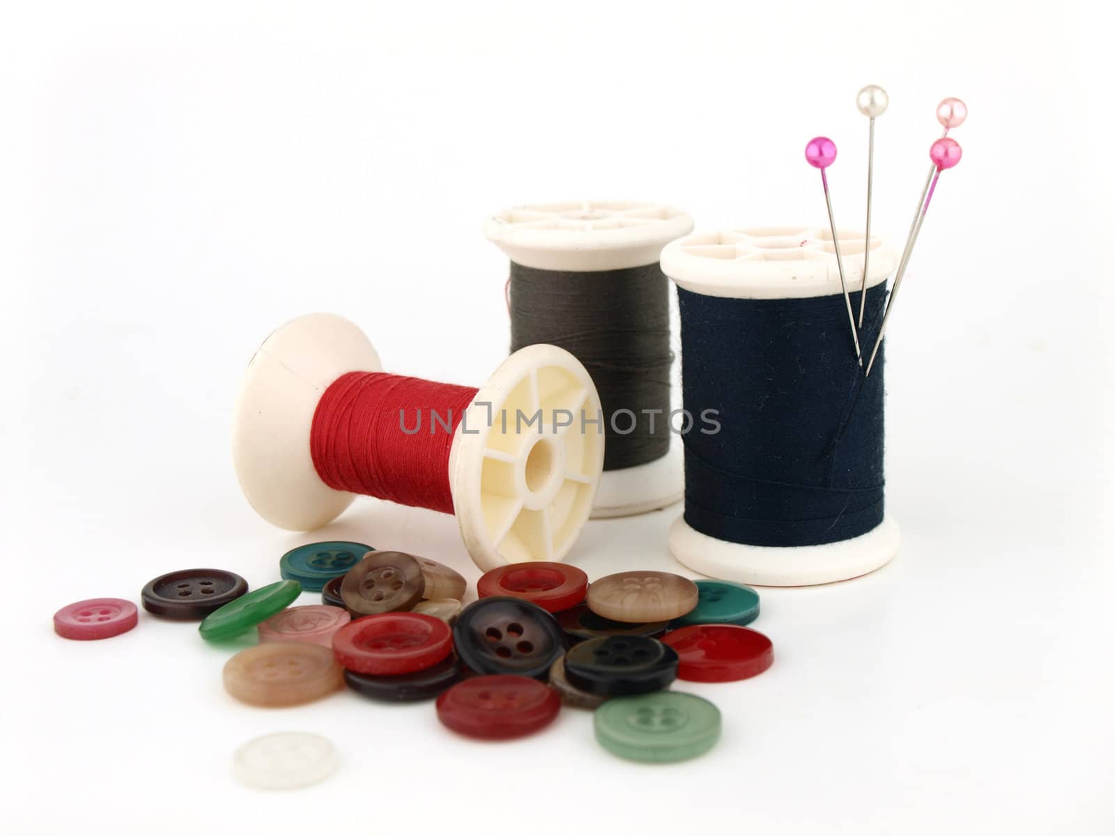 a spool of thread, needle and button on white  