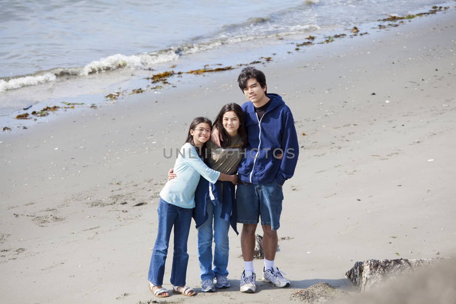 Brother and sisters standing on beach hugging