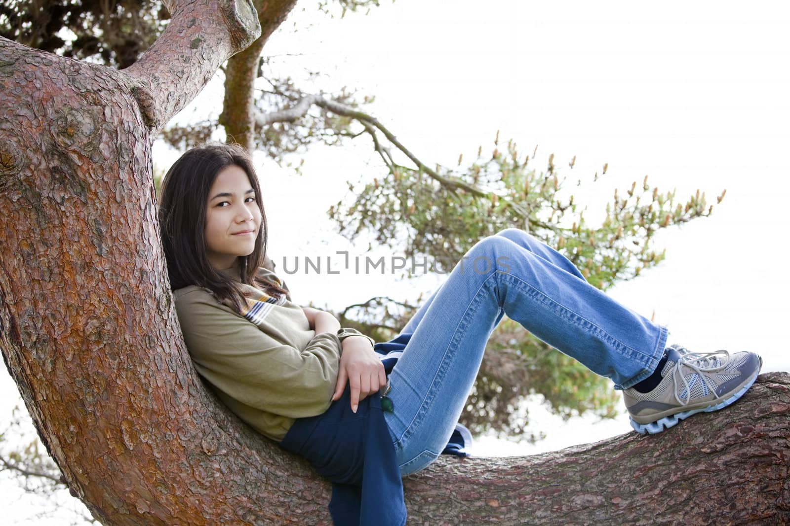 Young teen girl sitting on tree limb, relaxing