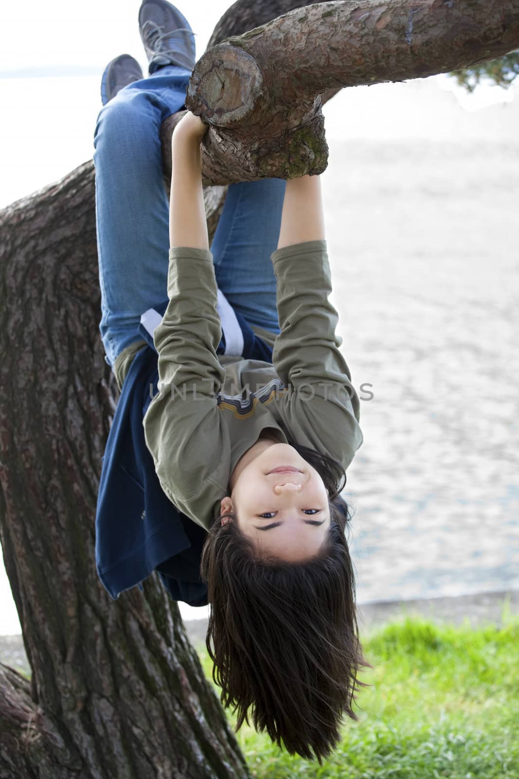 Young teen girl hanging upside down on tree limb