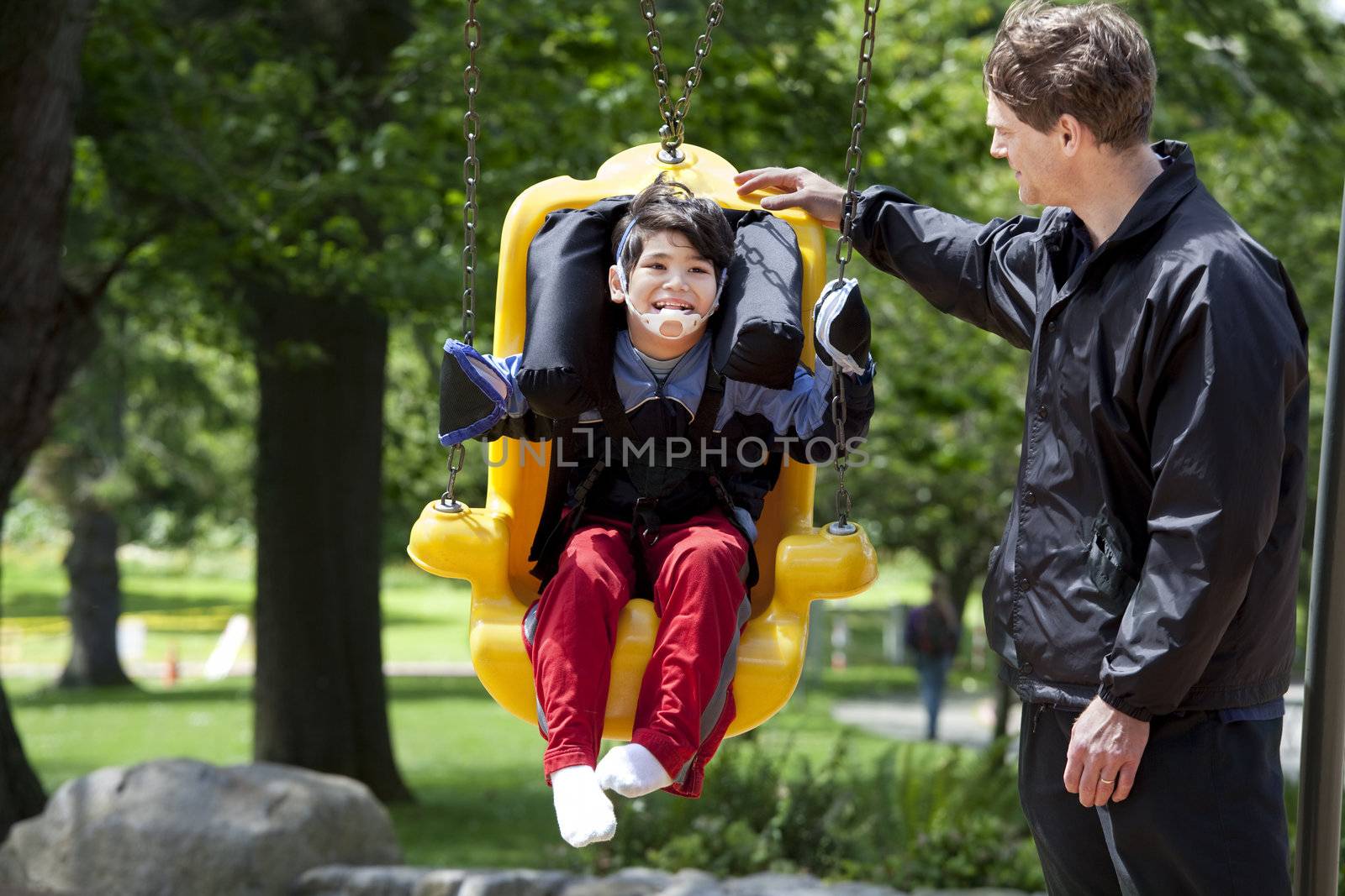 Father pushing disabled boy in special needs swing by jarenwicklund
