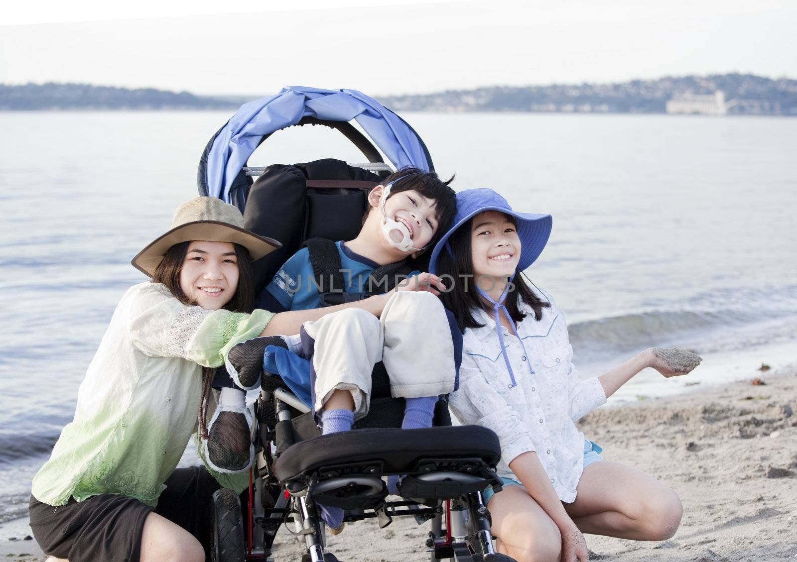 Sisters taking care of disabled brother in wheelchair on beach