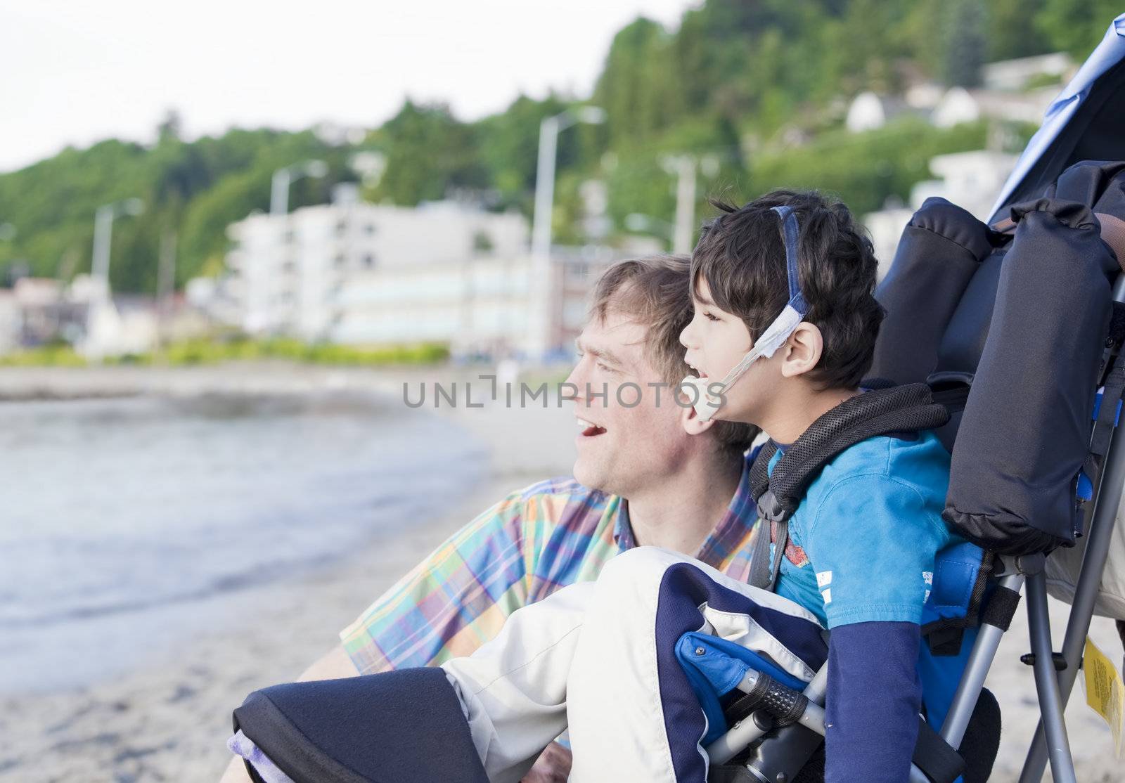 Father and disabled five year old son  on beach, looking out over water