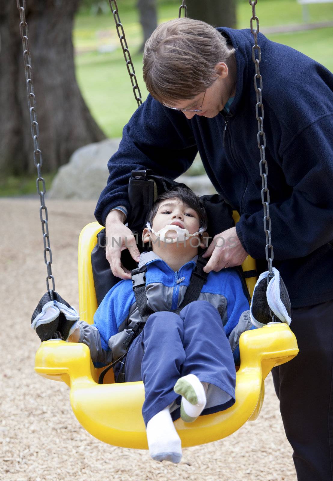 Father pushing disabled son  on handicap swing by jarenwicklund