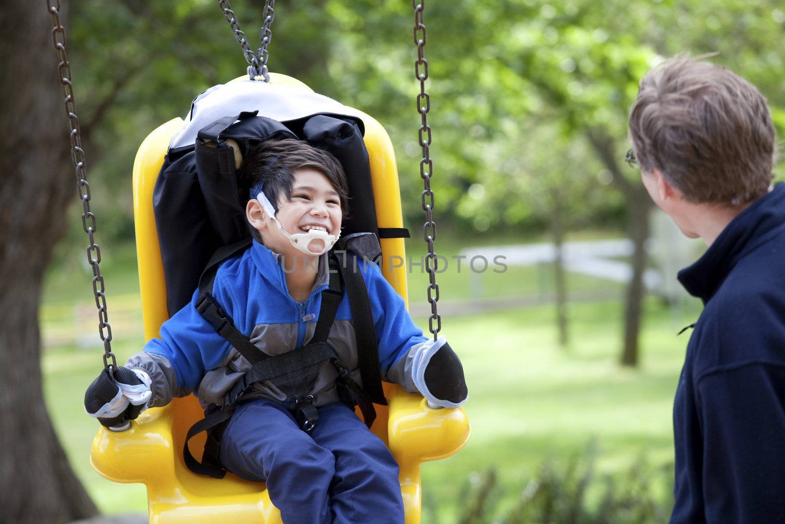 Father pushing disabled son  on yellow handicap swing