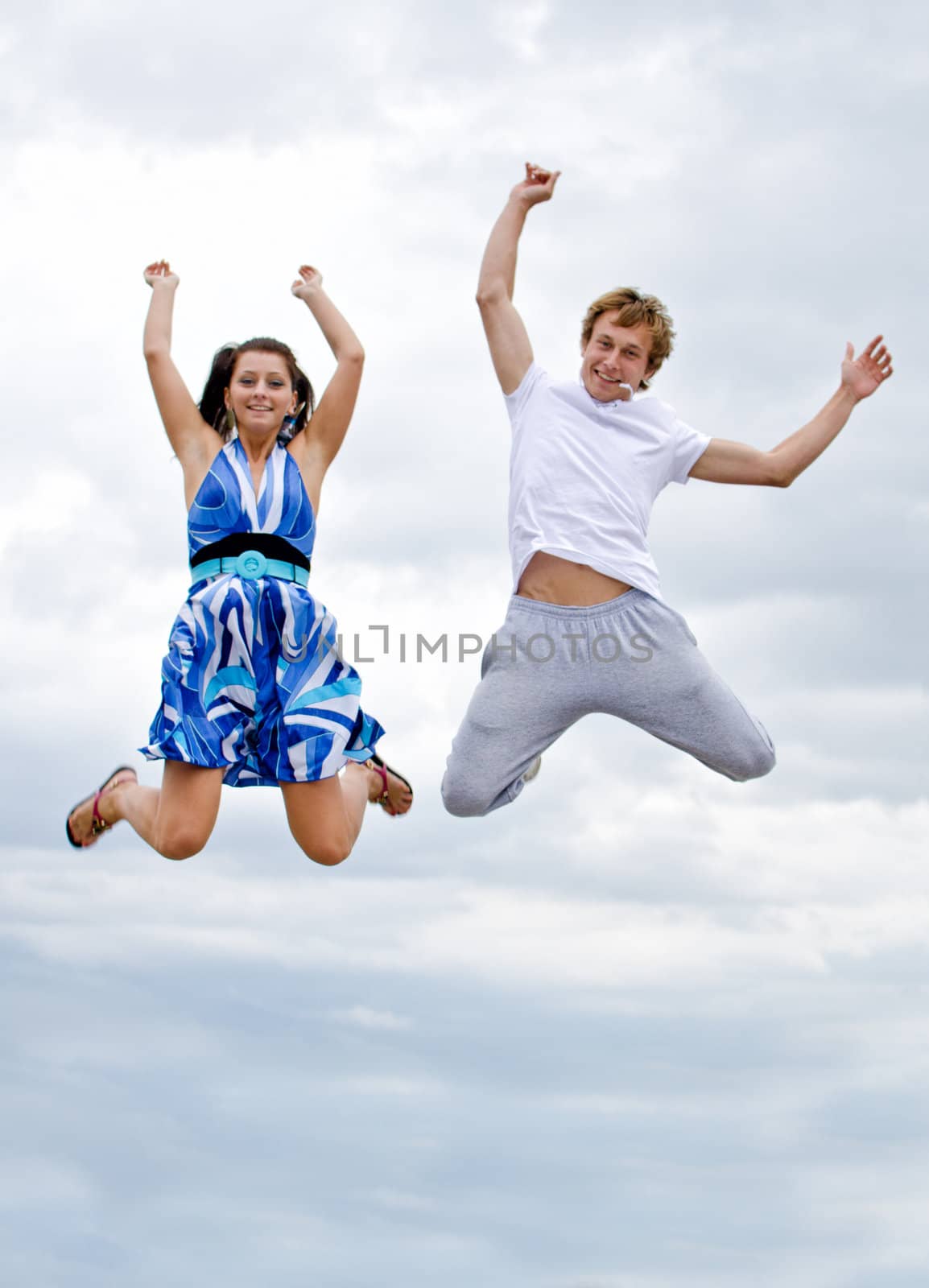 Portrait of a happy young couple jumping in air against sky.