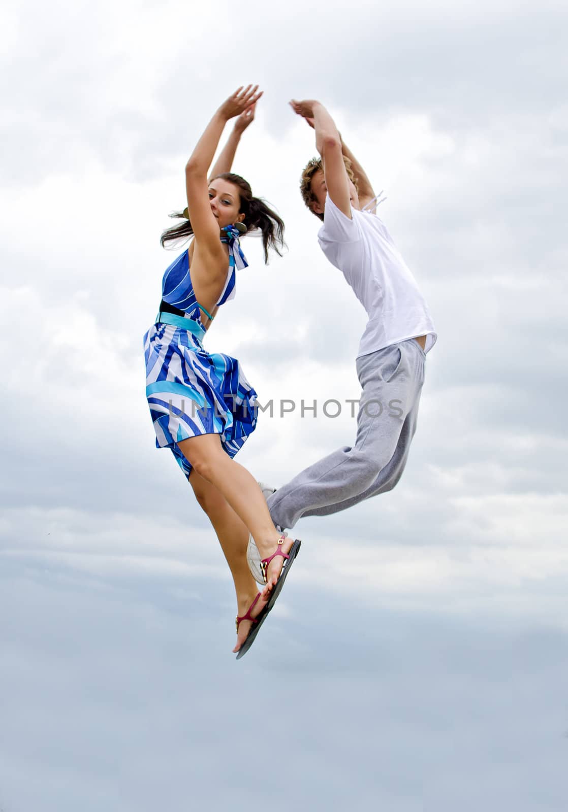 Portrait of a happy young couple jumping in air against sky.