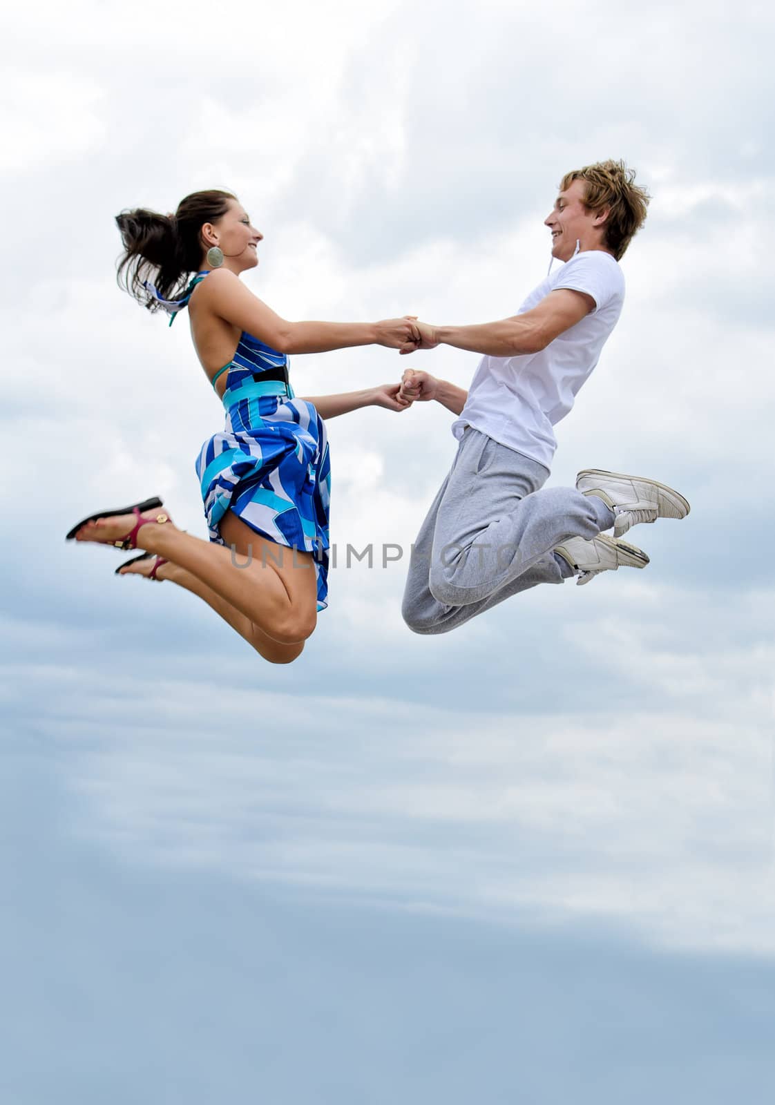 Portrait of a happy young couple jumping in air against sky.