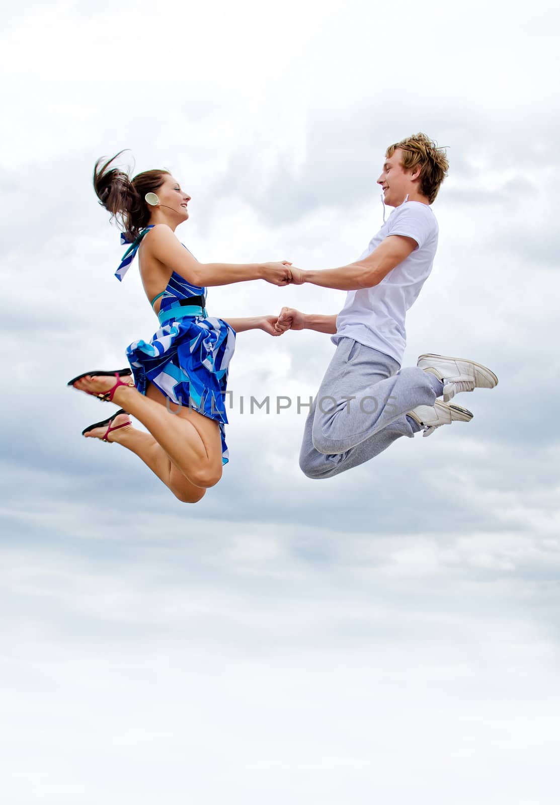 Portrait of a happy young couple jumping in air against sky.