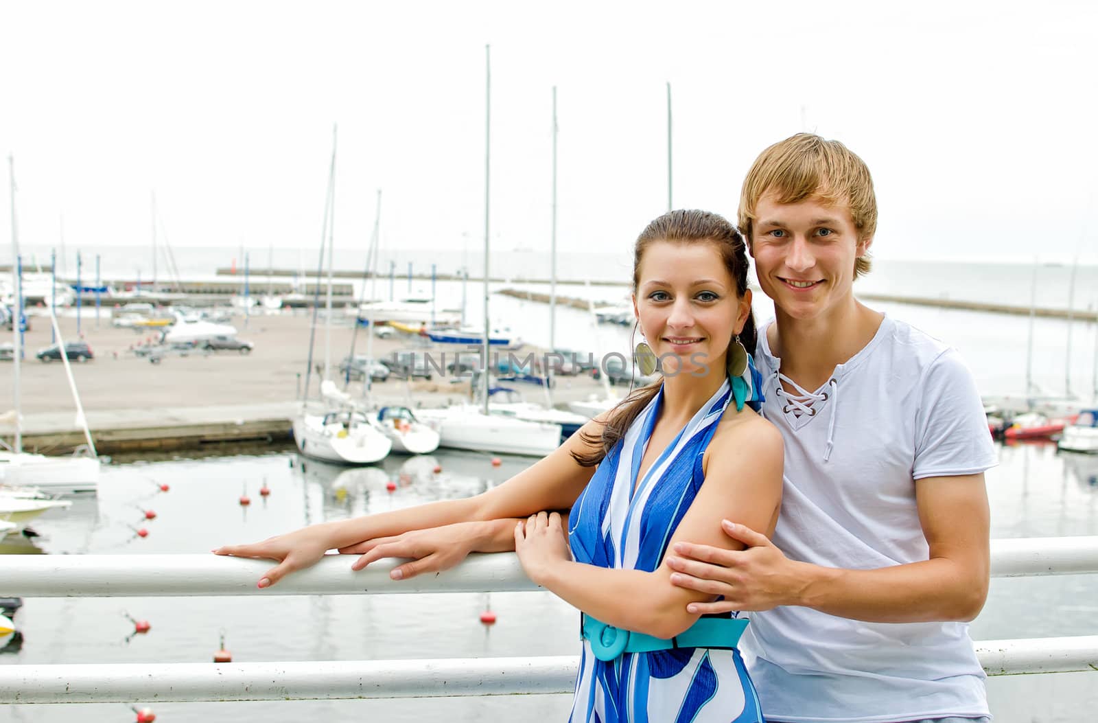 Attractive couple against pier with yachts.