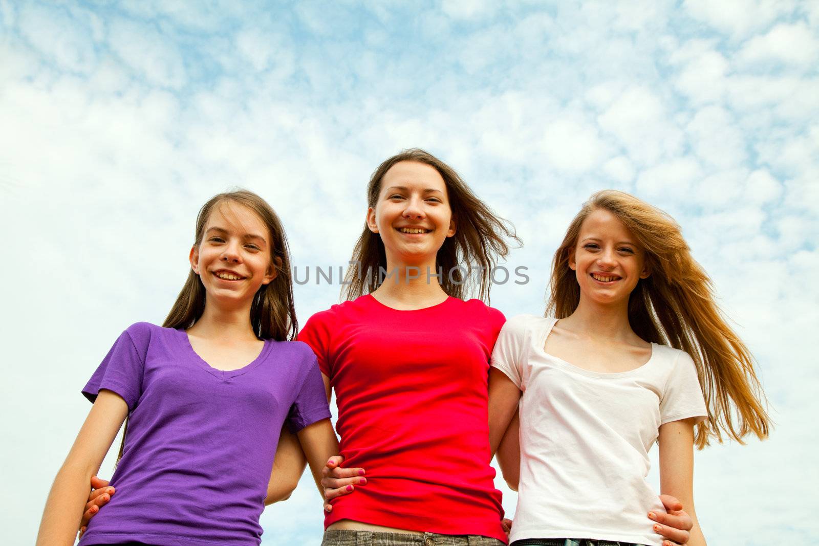 Three teen cheerful girls against blue sky