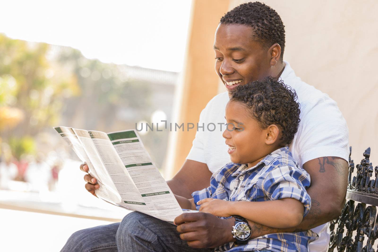 Happy African American Father and Mixed Race Son Having Fun Reading Park Brochure Outside.