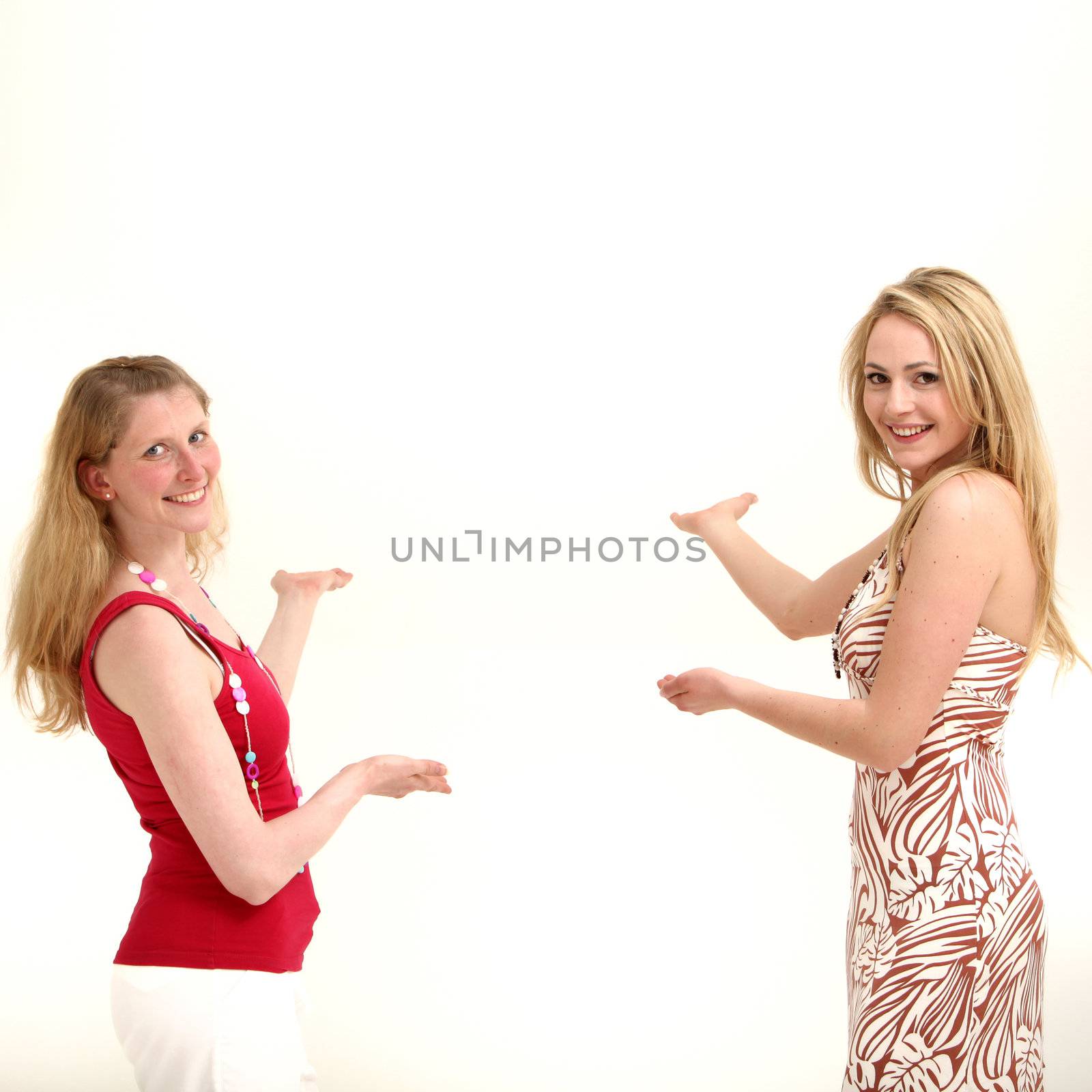 Two attractive friendly women standing facing each other with their palms out and other hands pointing to copyspace behind them as they coordinate a product placement concept