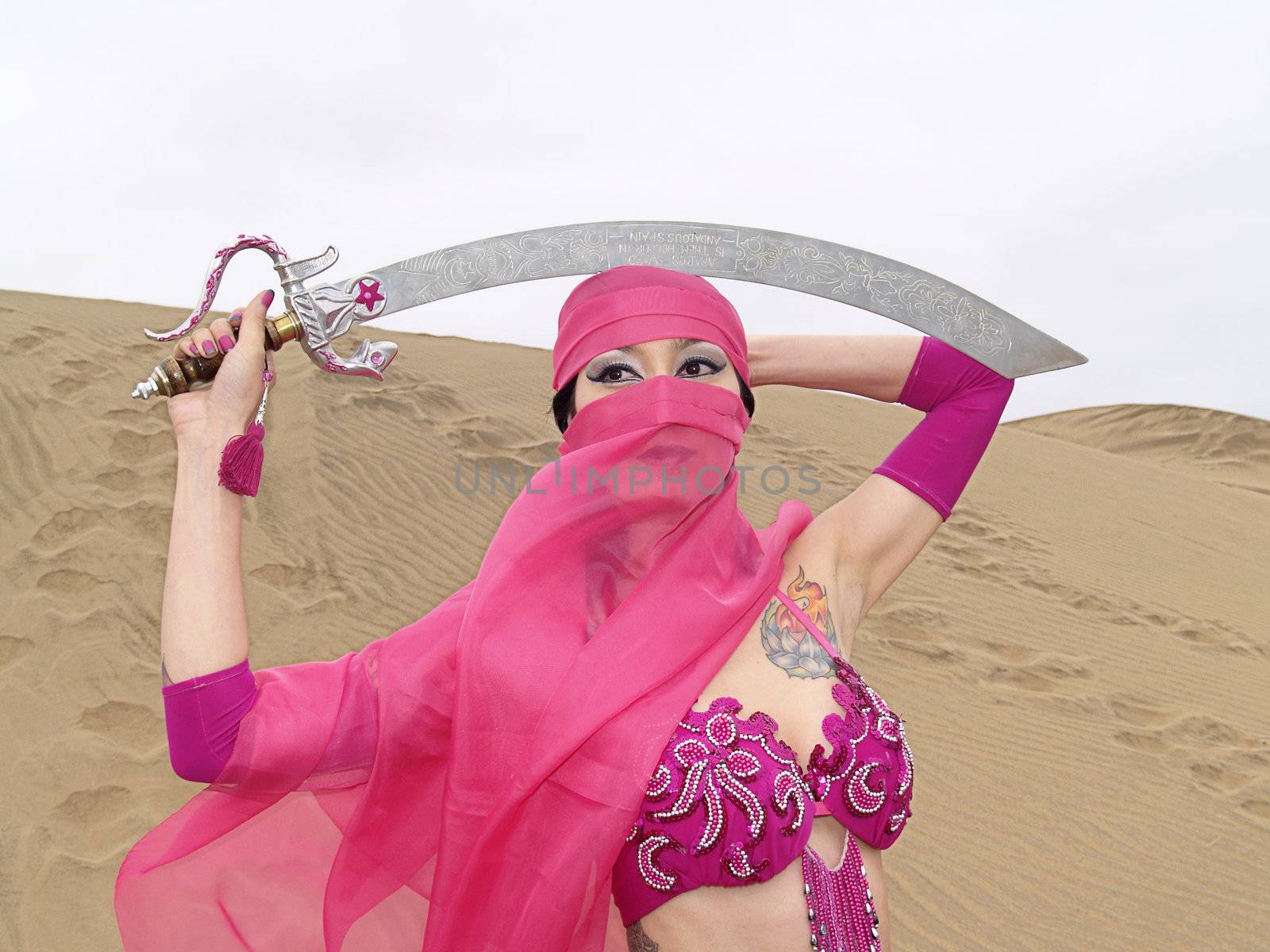 Portrait of a young veiled woman at desert with a sabre over her head