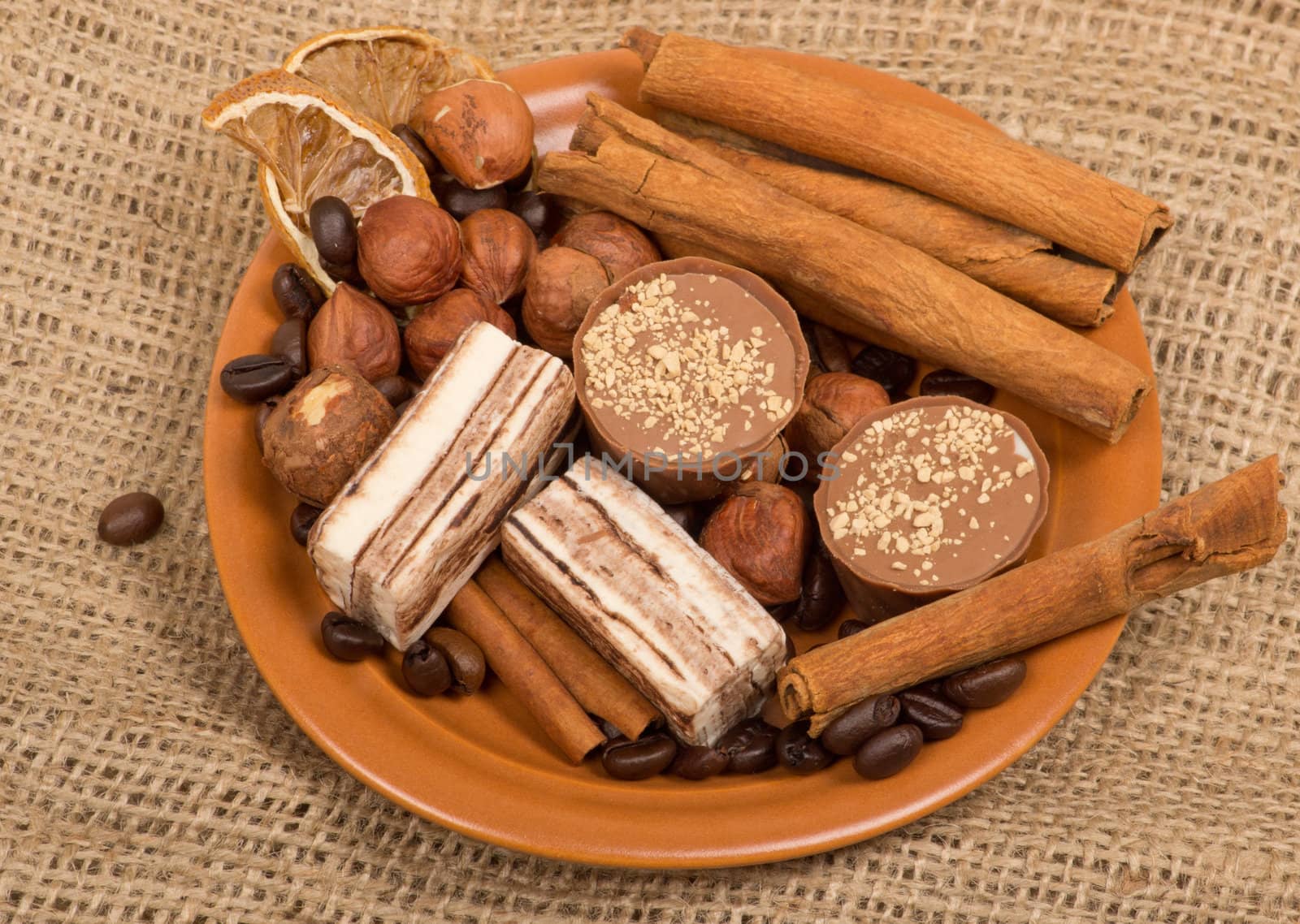 Sweets, cinnamon, nuts and coffee beans on a saucer, on burlap background.