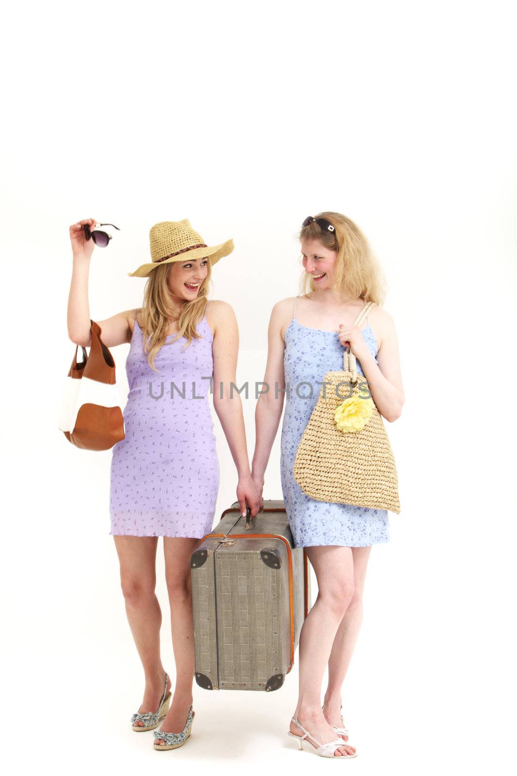 Two attractive female friends or sisters dressed in summer outfits off on their travels carrying a large suitcase between them