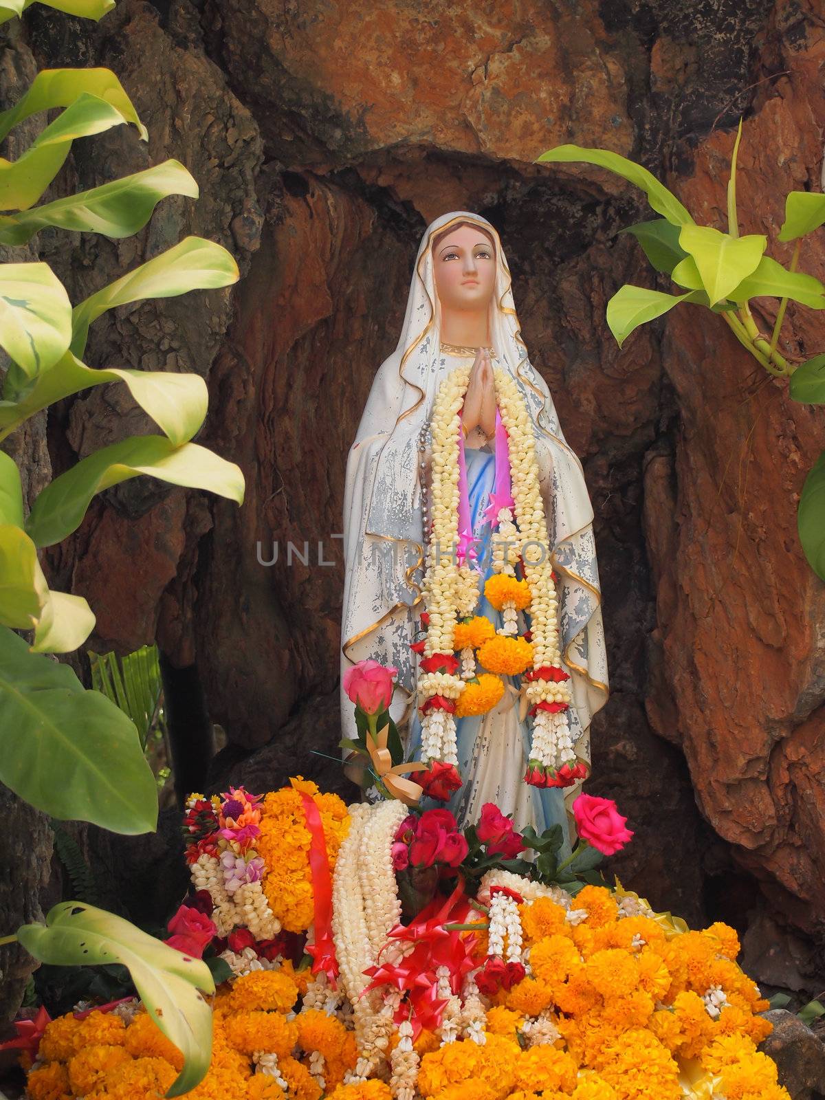 Virgin mary statue with garlands in cave.