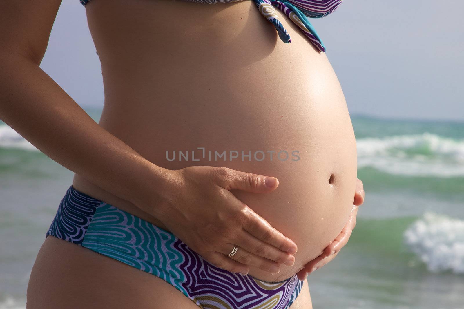 Closeup of hands holding big pregnant belly in front of the sea by fmarsicano