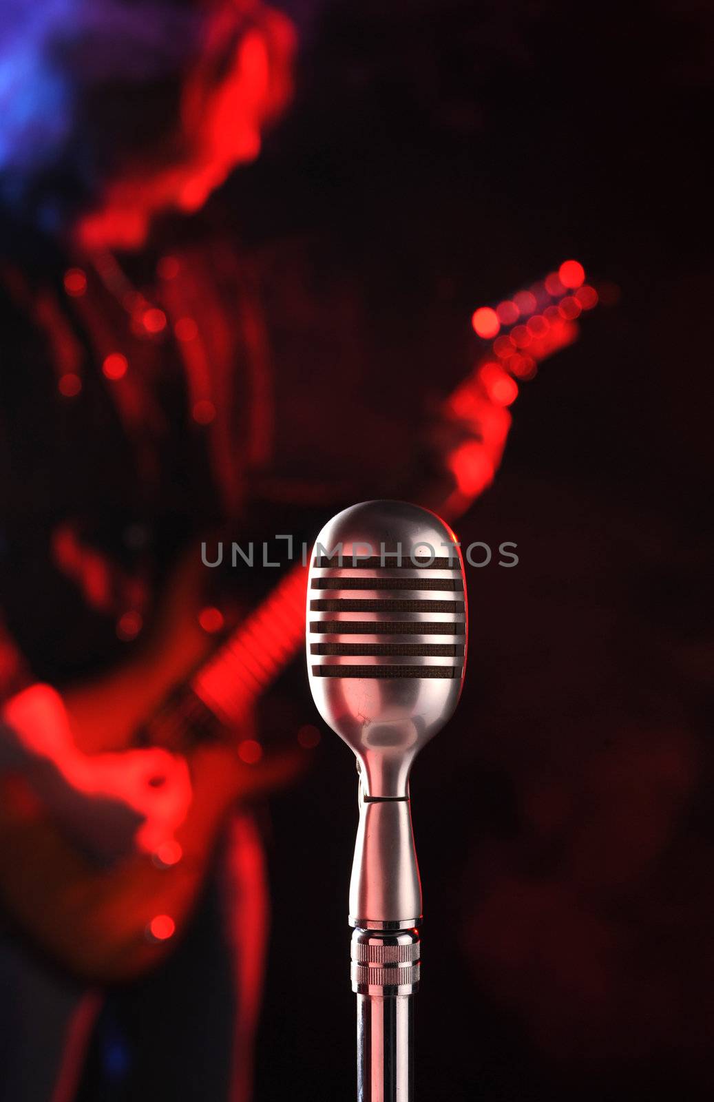 old microphone in the foreground with a guitarist in the background