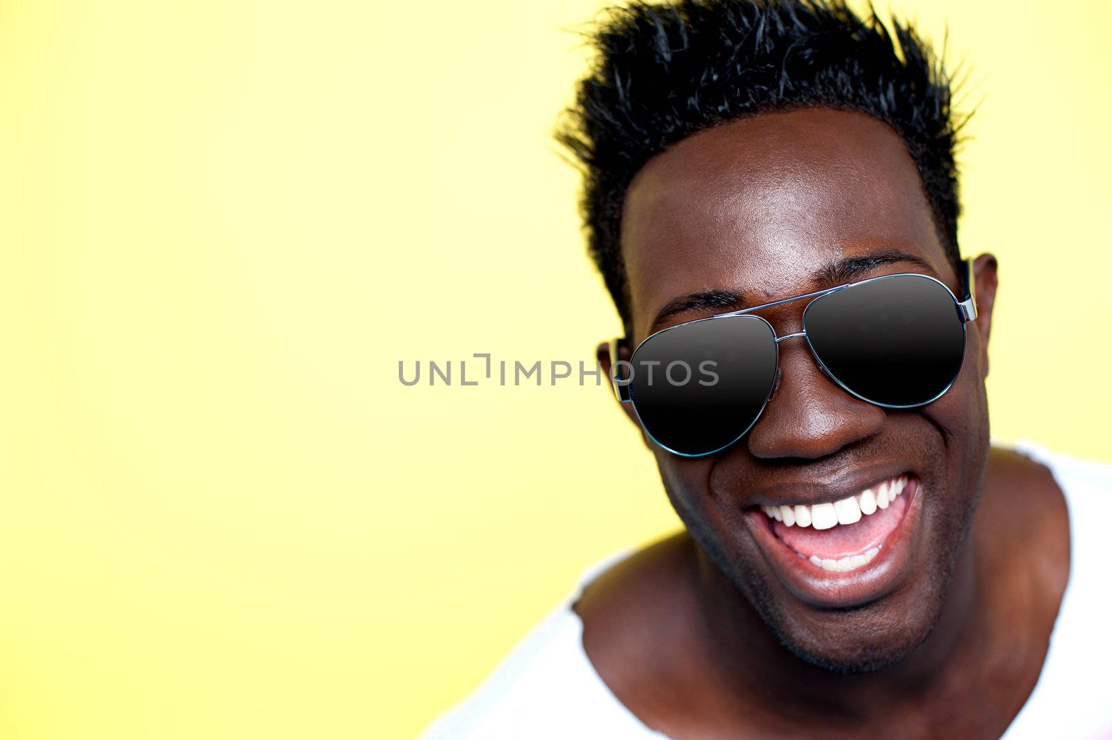 Closeup of joyful young african guy in sunglasses. All on yellow background