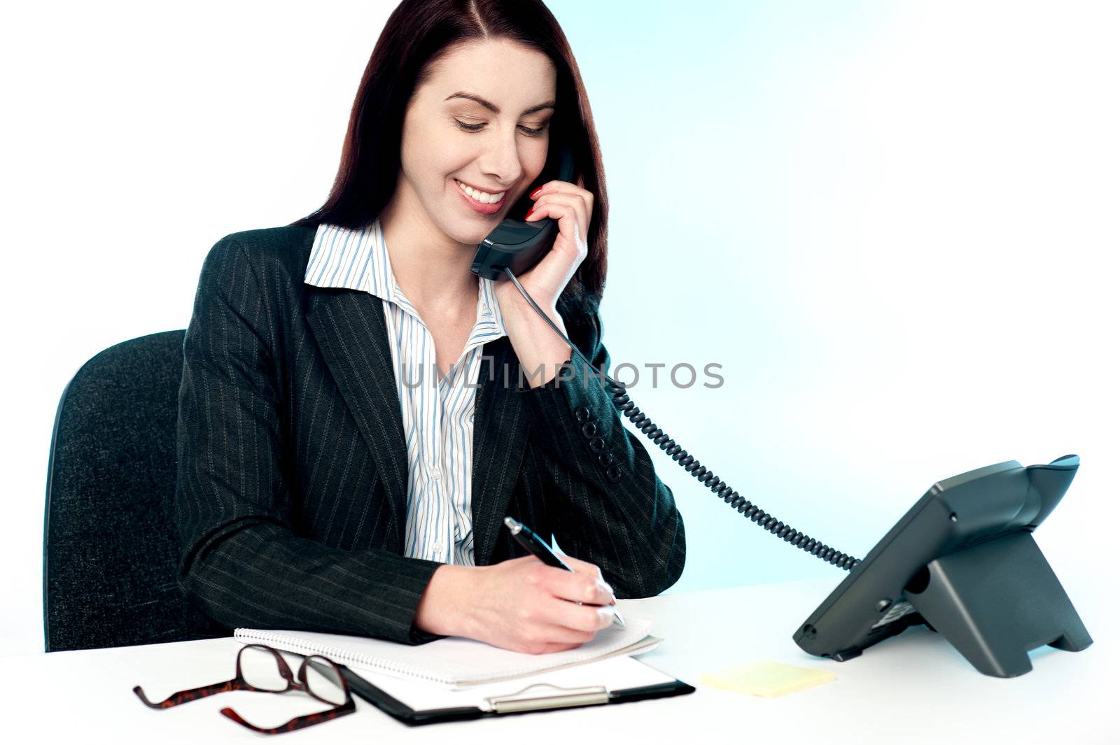 Smiling female operator attending clients call and writing key points as directed