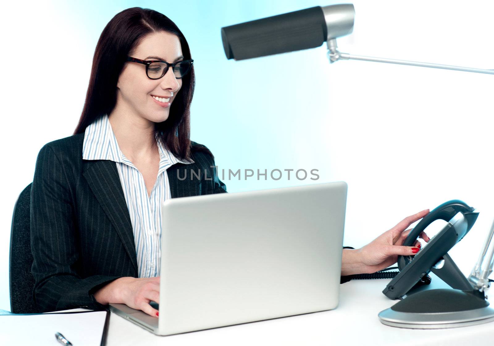 Female secretary answering phone call in office. Working on laptop