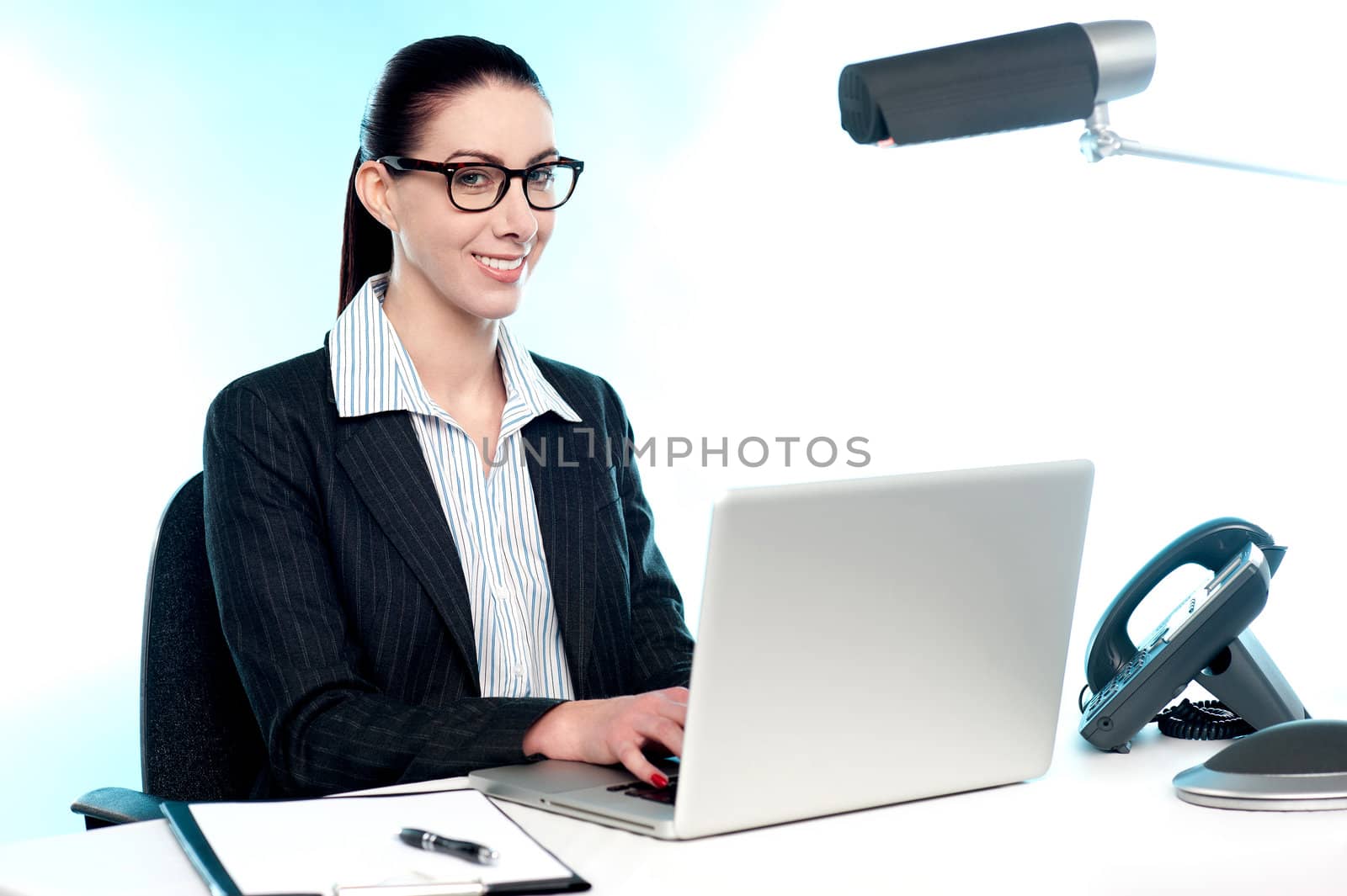 Smiling female secretary working on laptop. Indoor office shot