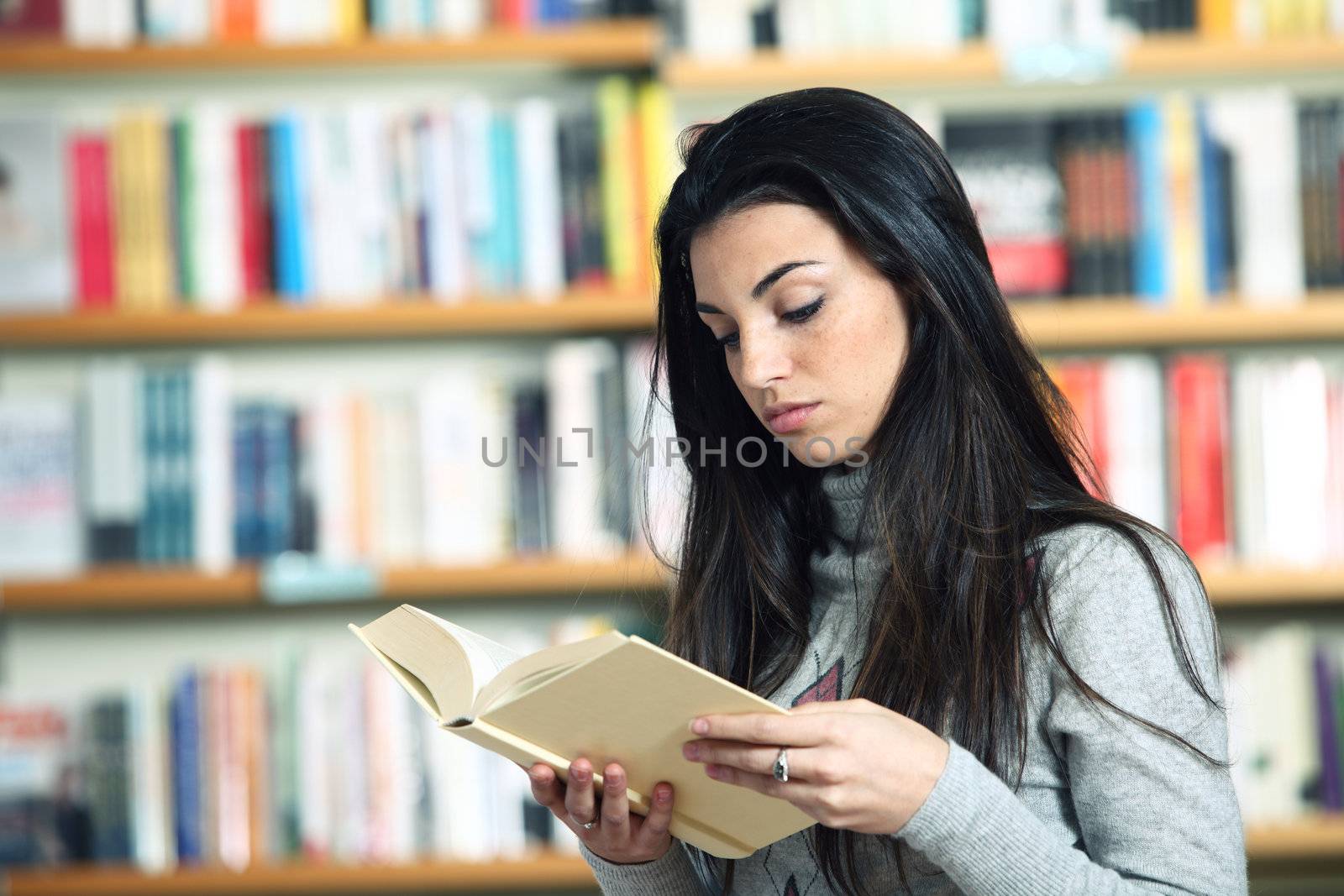 female student reading a book in library by stokkete