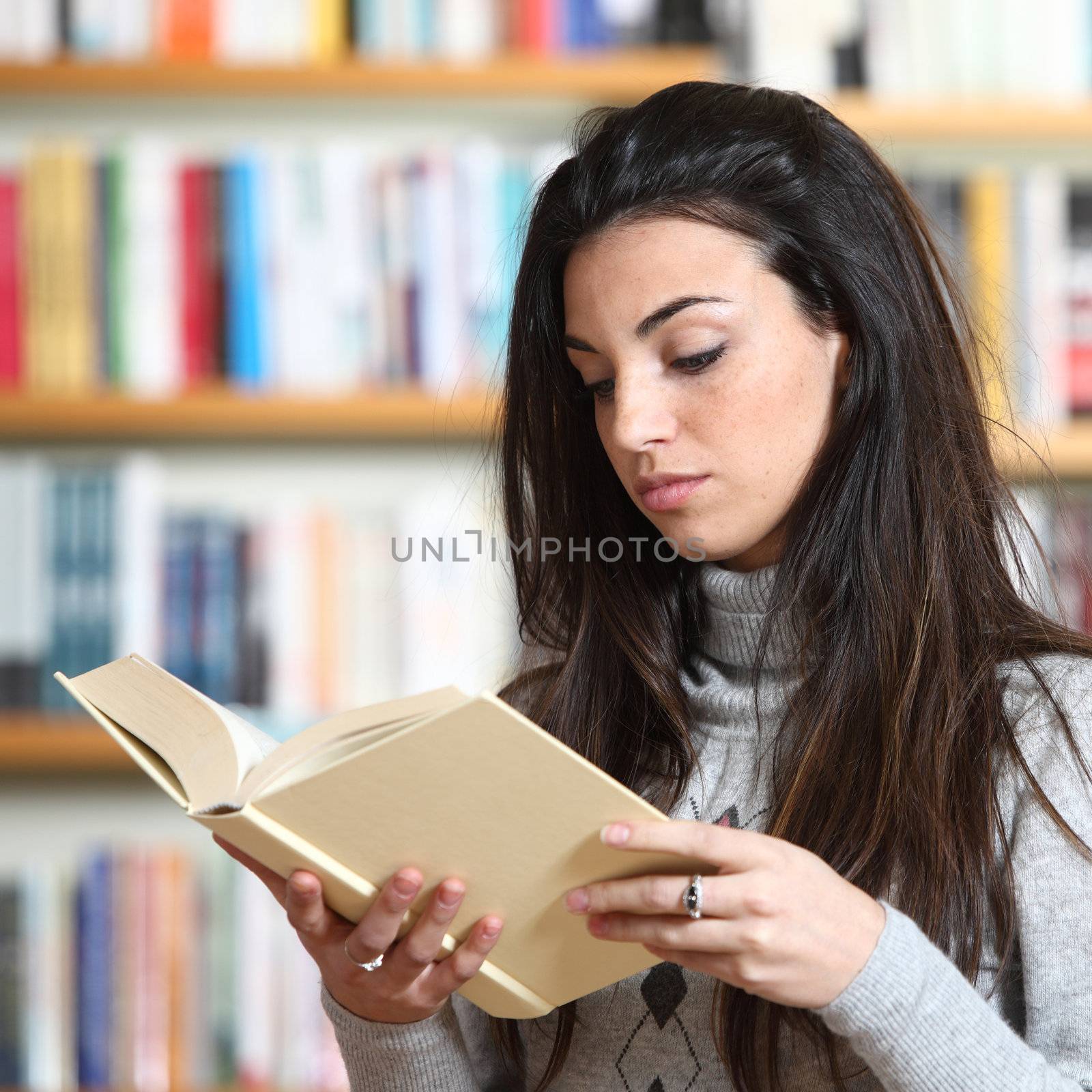 female student reading a book in library by stokkete