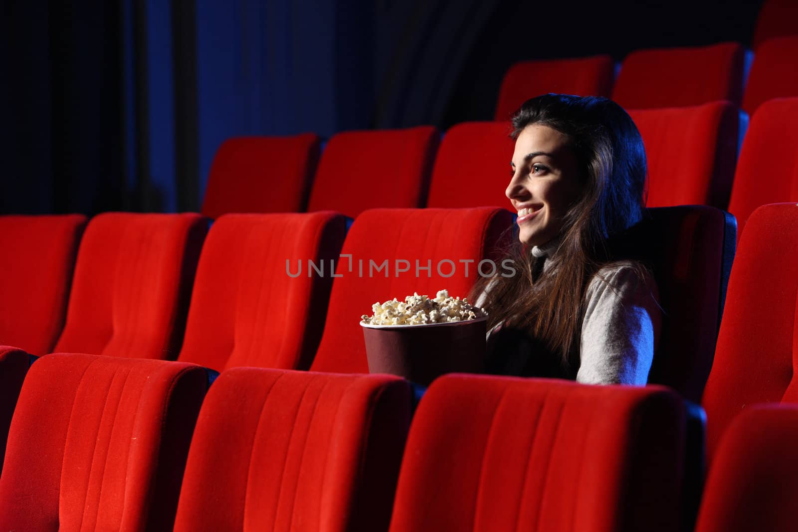 a pretty young woman sitting in an empty theater, she eats popco by stokkete