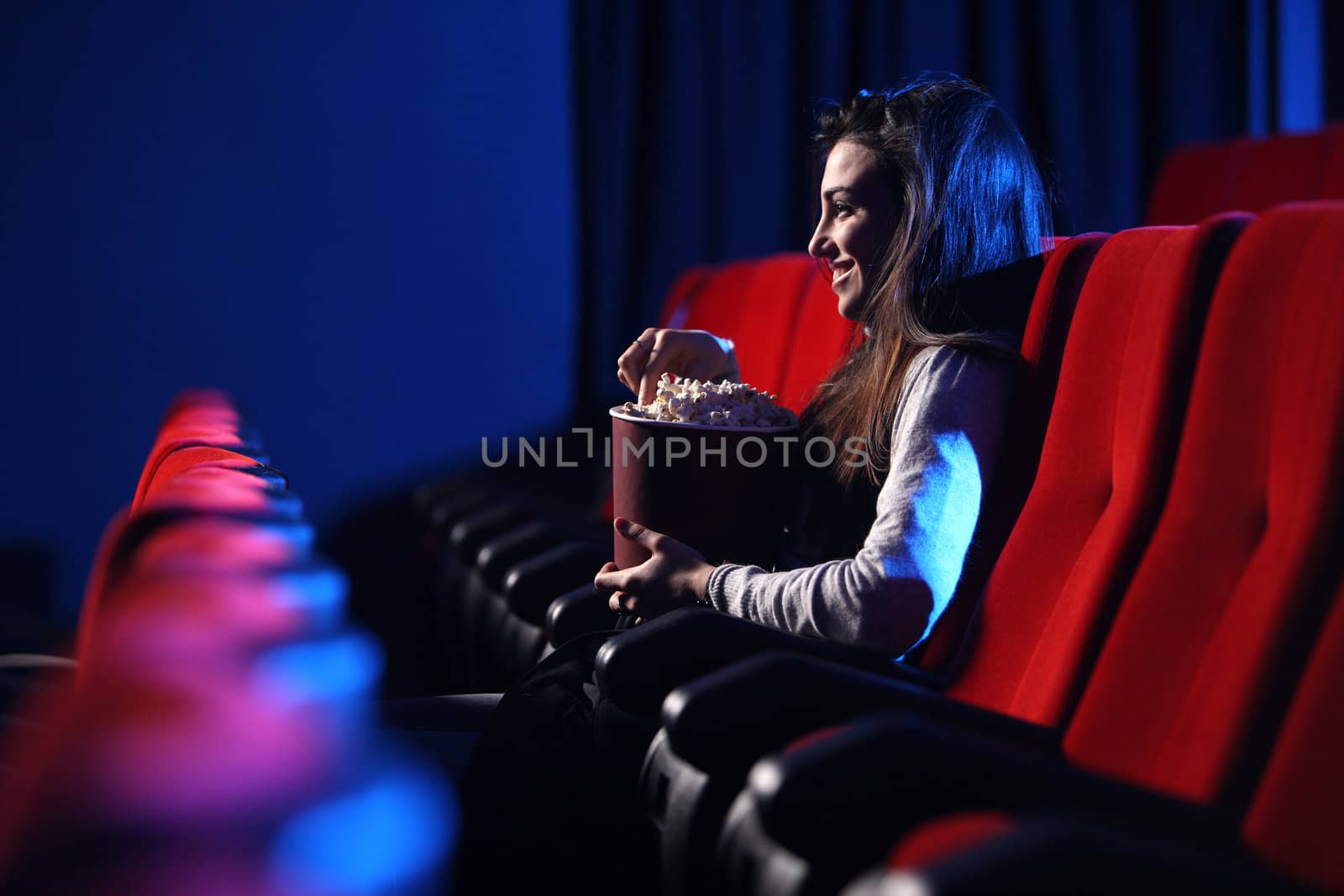 funny movie: portrait of a pretty young woman, eats popcorn and smiles, side view