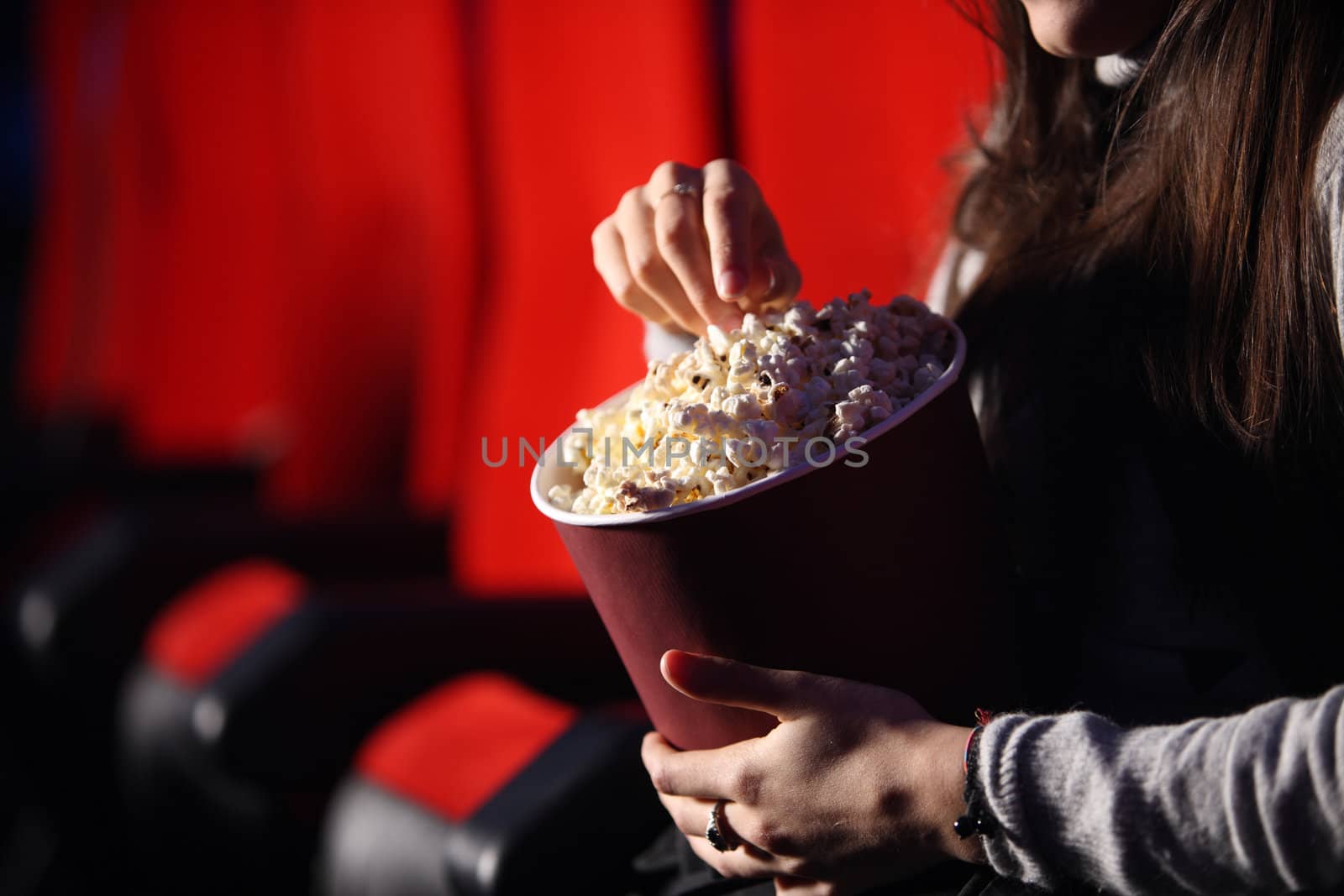 close up of the hands of a girl in a movie theater, she eats popcorn