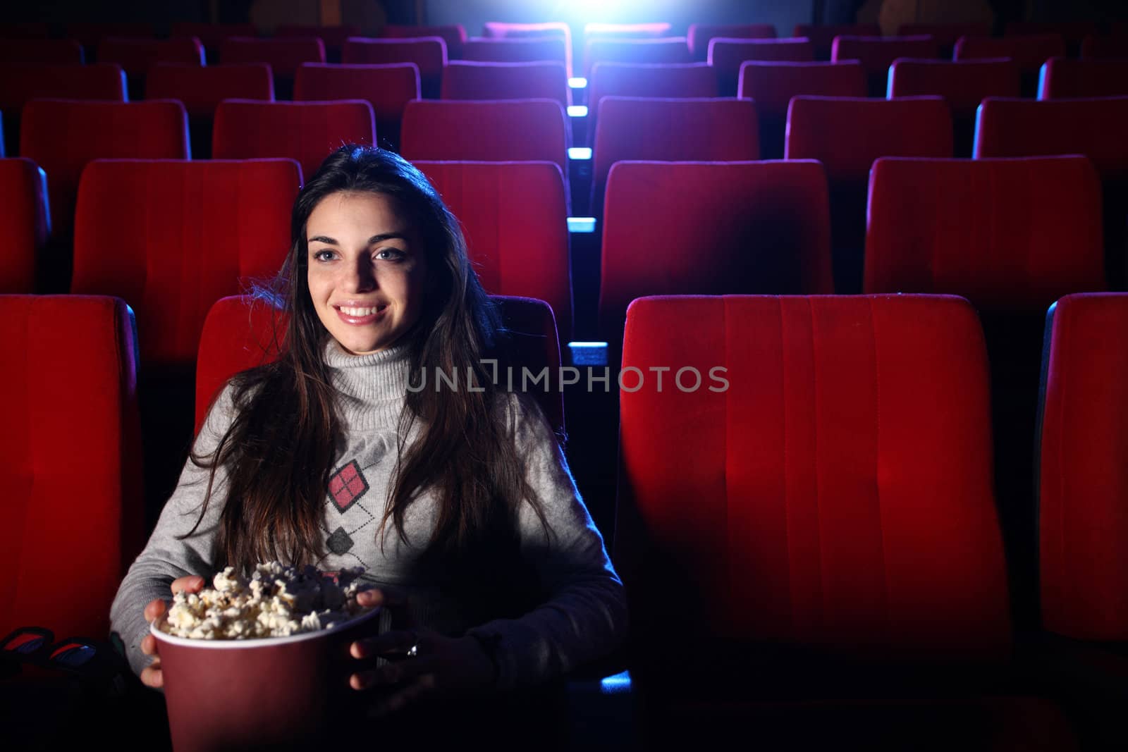 a pretty girl alone sitting in a empty movie theater, she eats popcorn and smiles