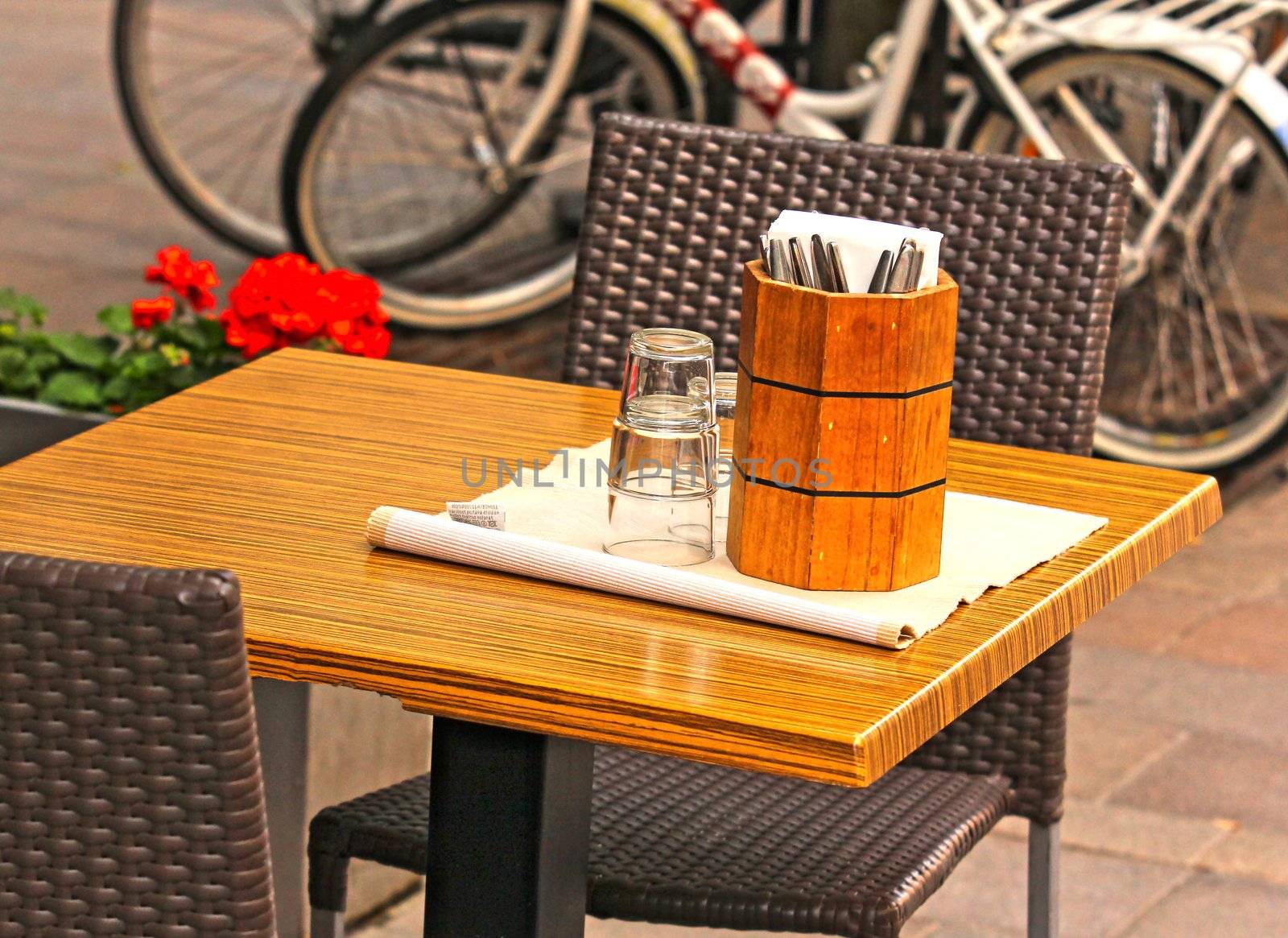 Patio with table and chairs, knifes and forks in a wooden stand by Arvebettum