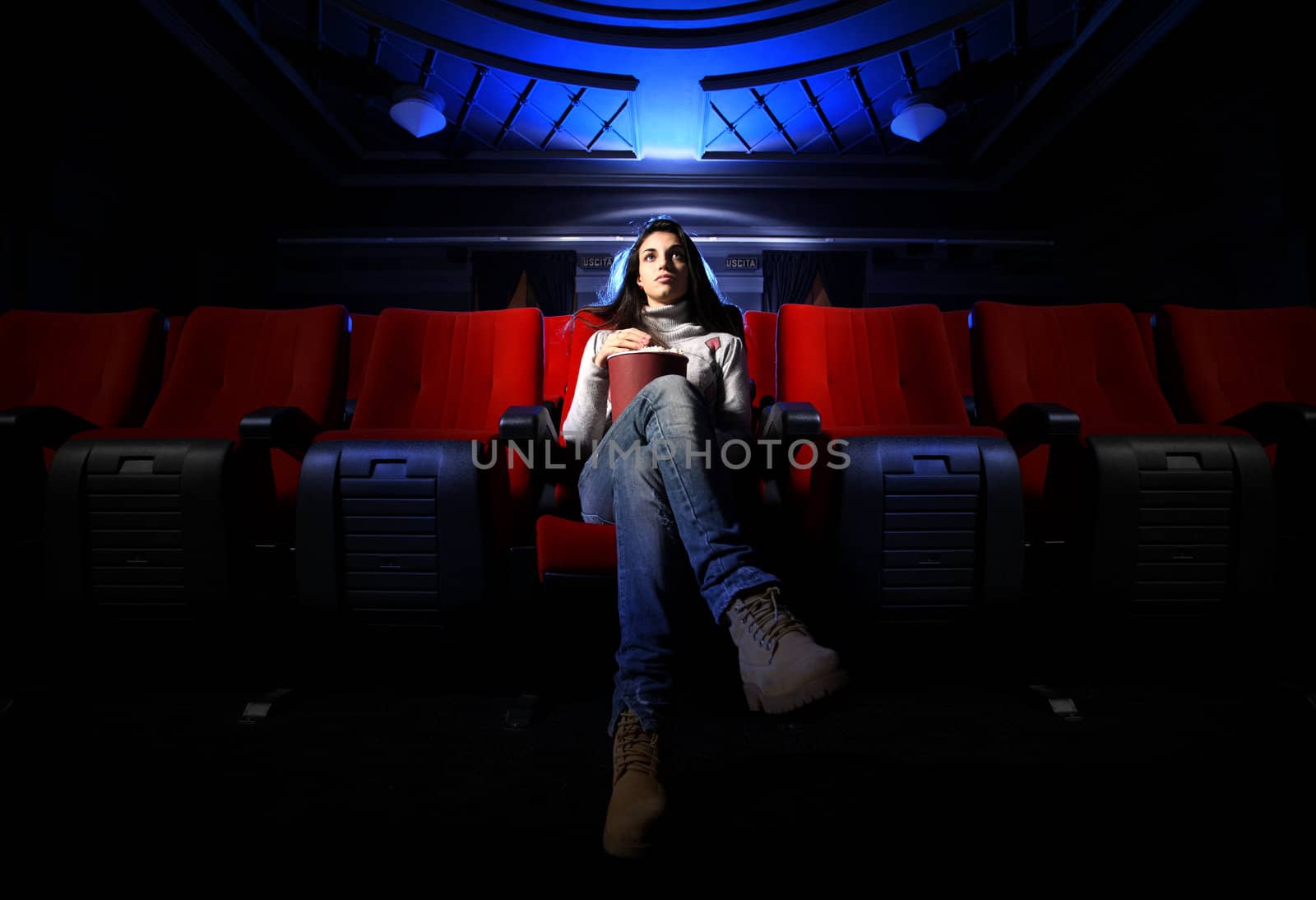 a pretty young woman is sitting alone in an empty theater, waiting for the movie