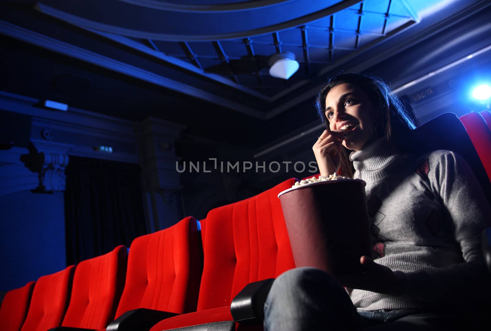 a pretty young woman sitting in an empty theater, she eats popcorn and smiles