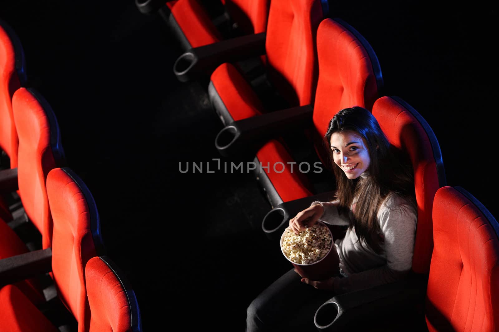 a pretty young woman sitting in an empty theater, eats popcorn and smiles, top view