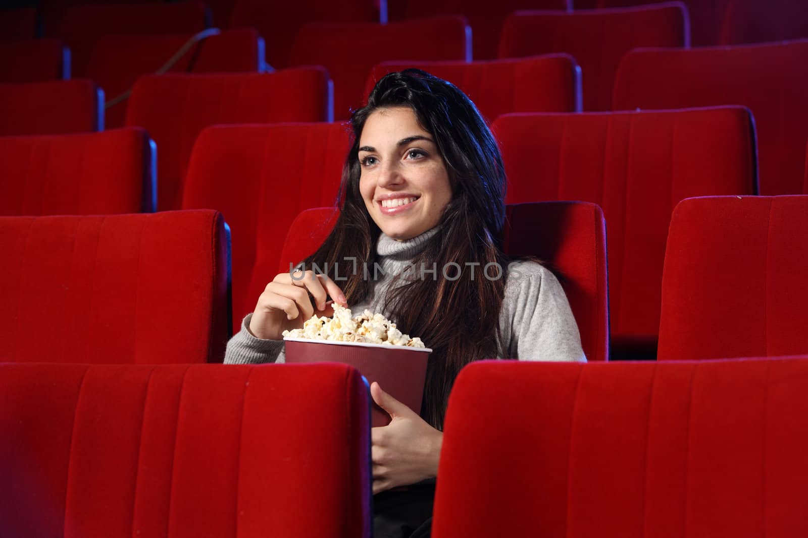 funny movie: portrait of a pretty girl in an empty theater, she eats popcorn and smiles