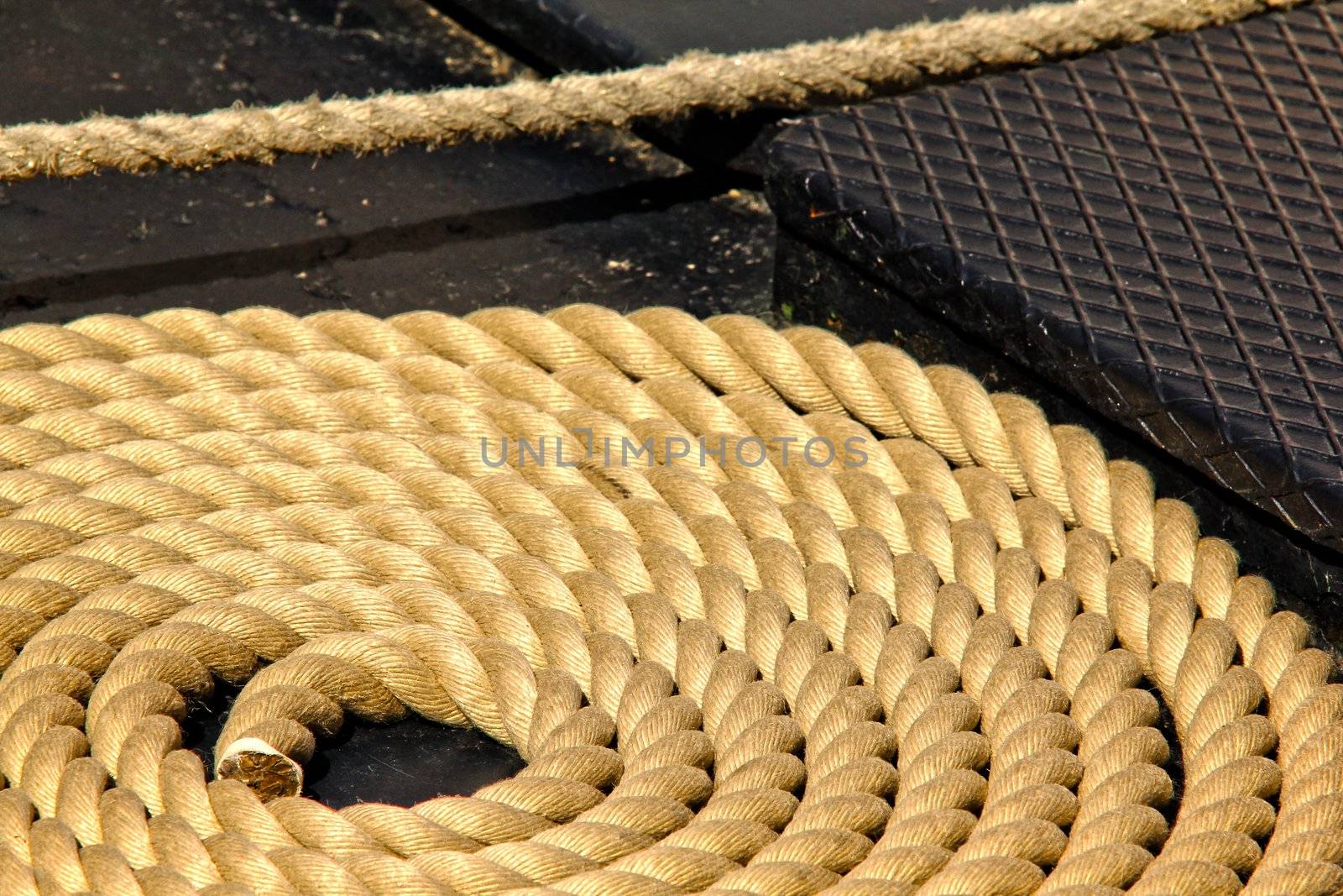 Close-up of an old frayed boat rope in circle, on the deck of a boat by Arvebettum