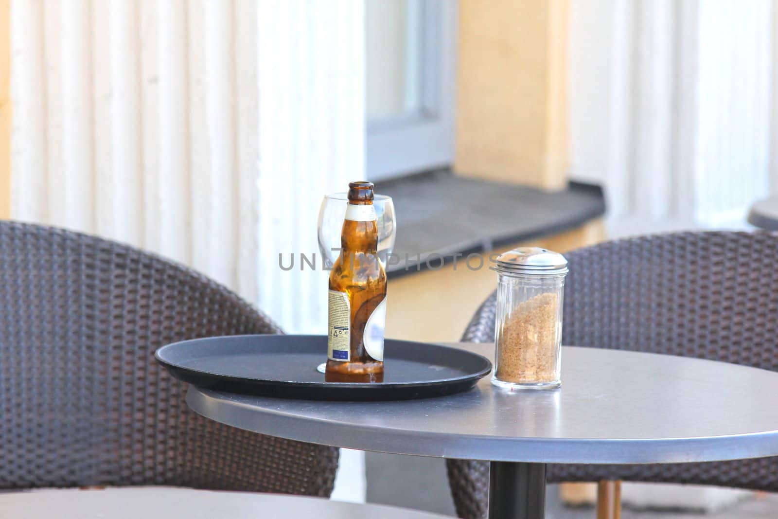 Restaurant outdoors, beer bottle on table, nobody around by Arvebettum