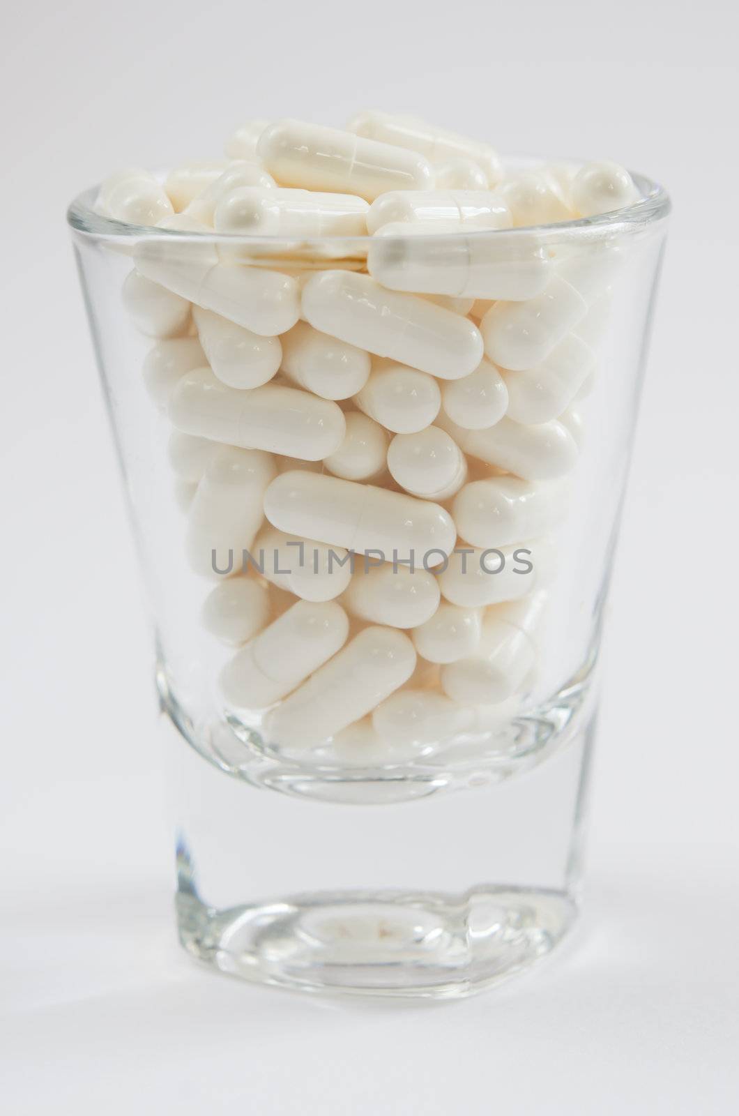 close up white pills  in glass  on white 