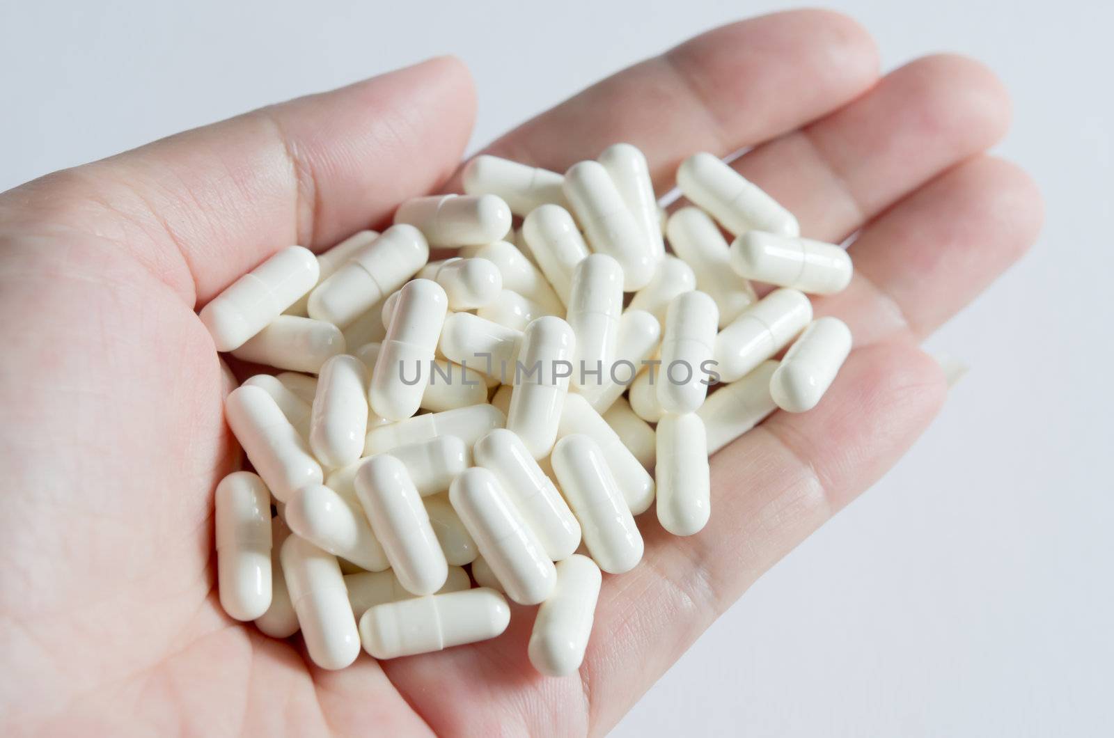 many white  pills spilling on hand with white background