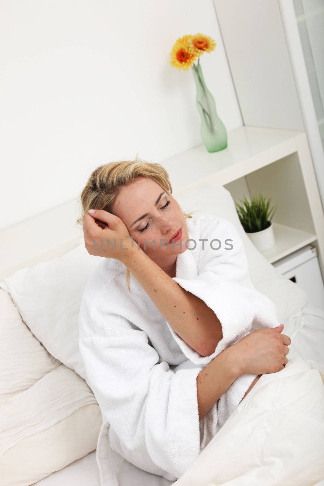 Beautiful woman dreaming as she slowly awakens while sitting in her bed in a white towelling gown