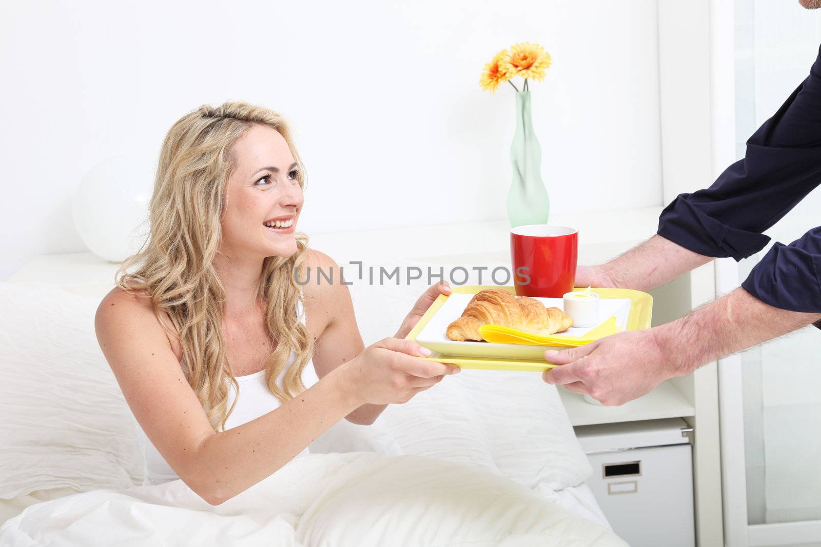 Beautiful blonde woman being treated to breakfast of croissant and coffee in bed