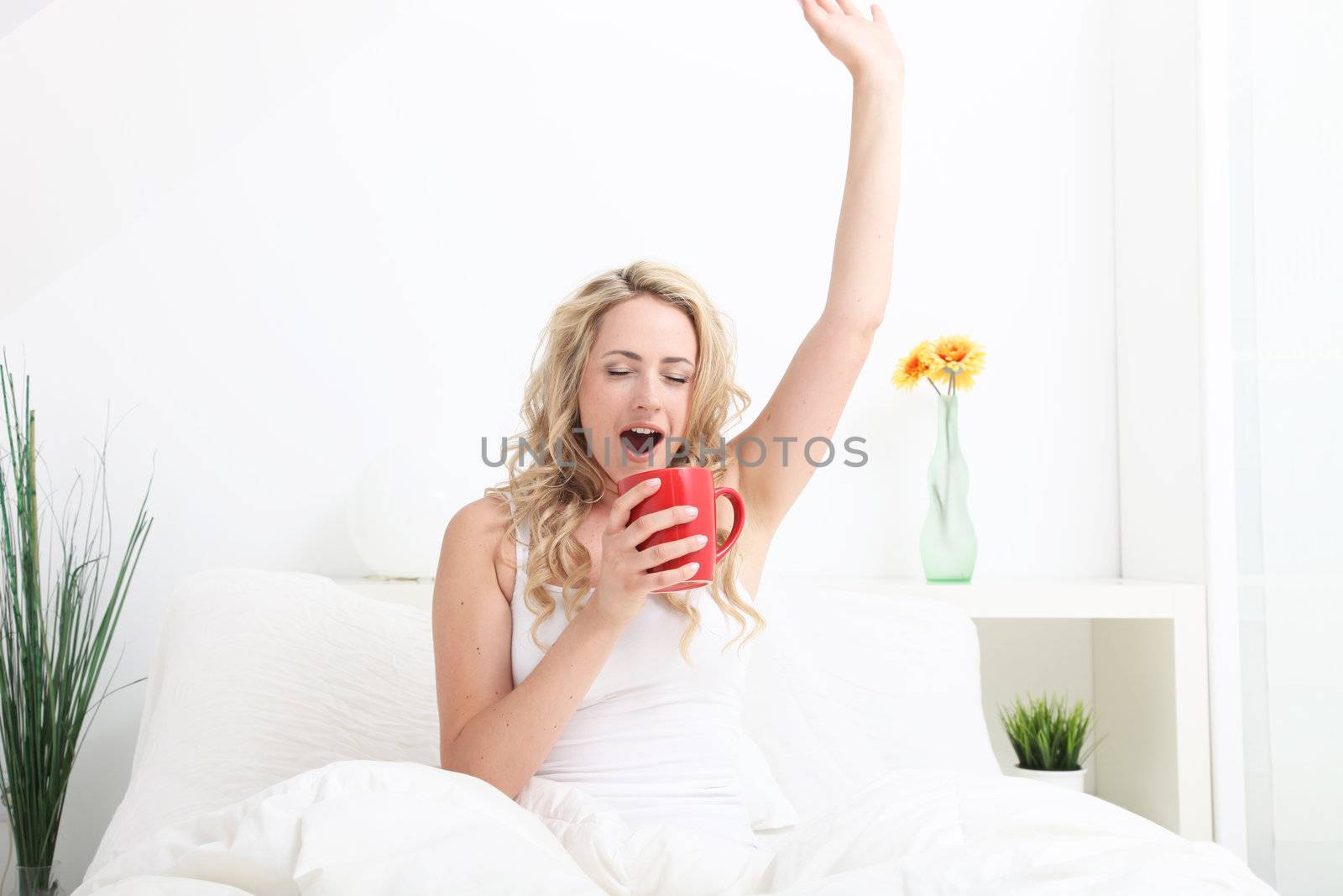 Languid woman yawning and stretching as she sits in bed drinking coffee