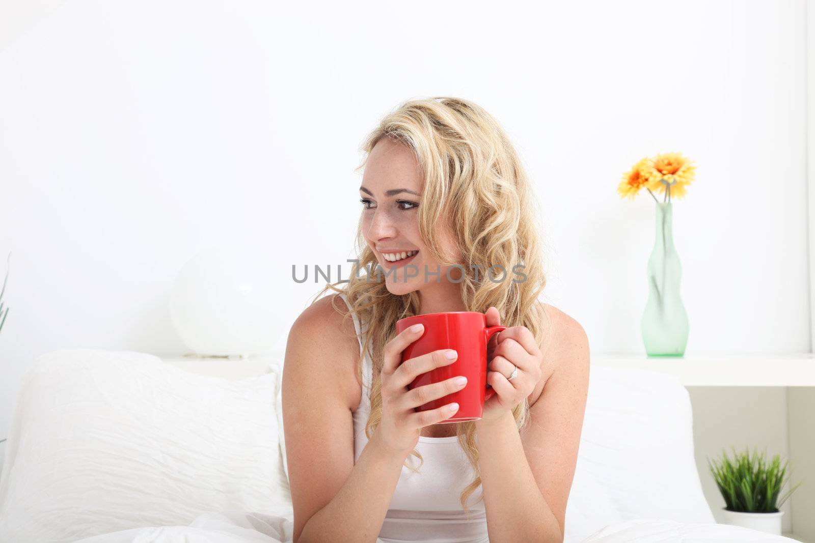 Happy smiling woman sitting in bed drinking coffee and looking sideways off frame across blank copyspace